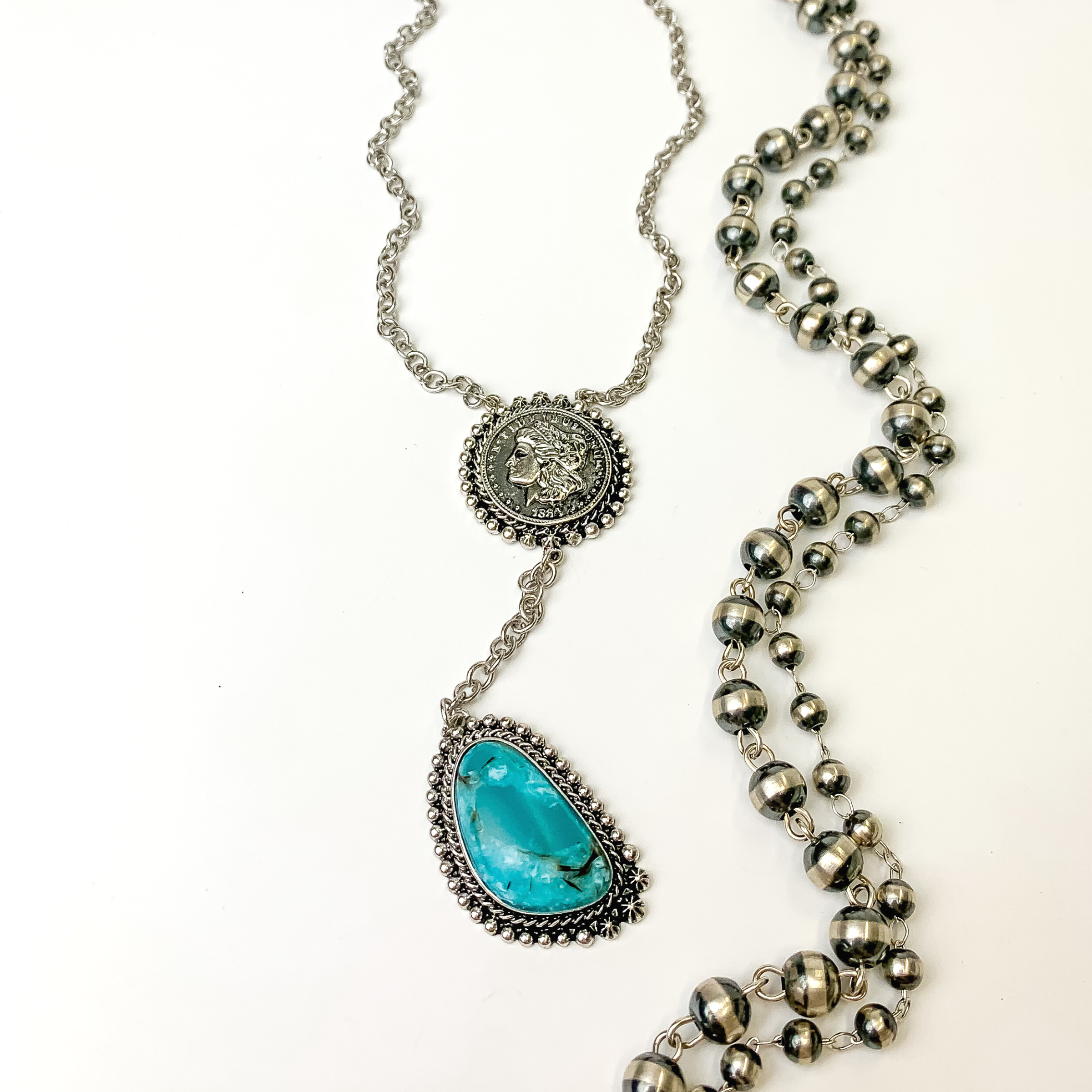 Silver chain, lariat necklace with a silver coin pendant and turquoise stone drop. This necklace is pictured on a white background with silver beads on the right side. 