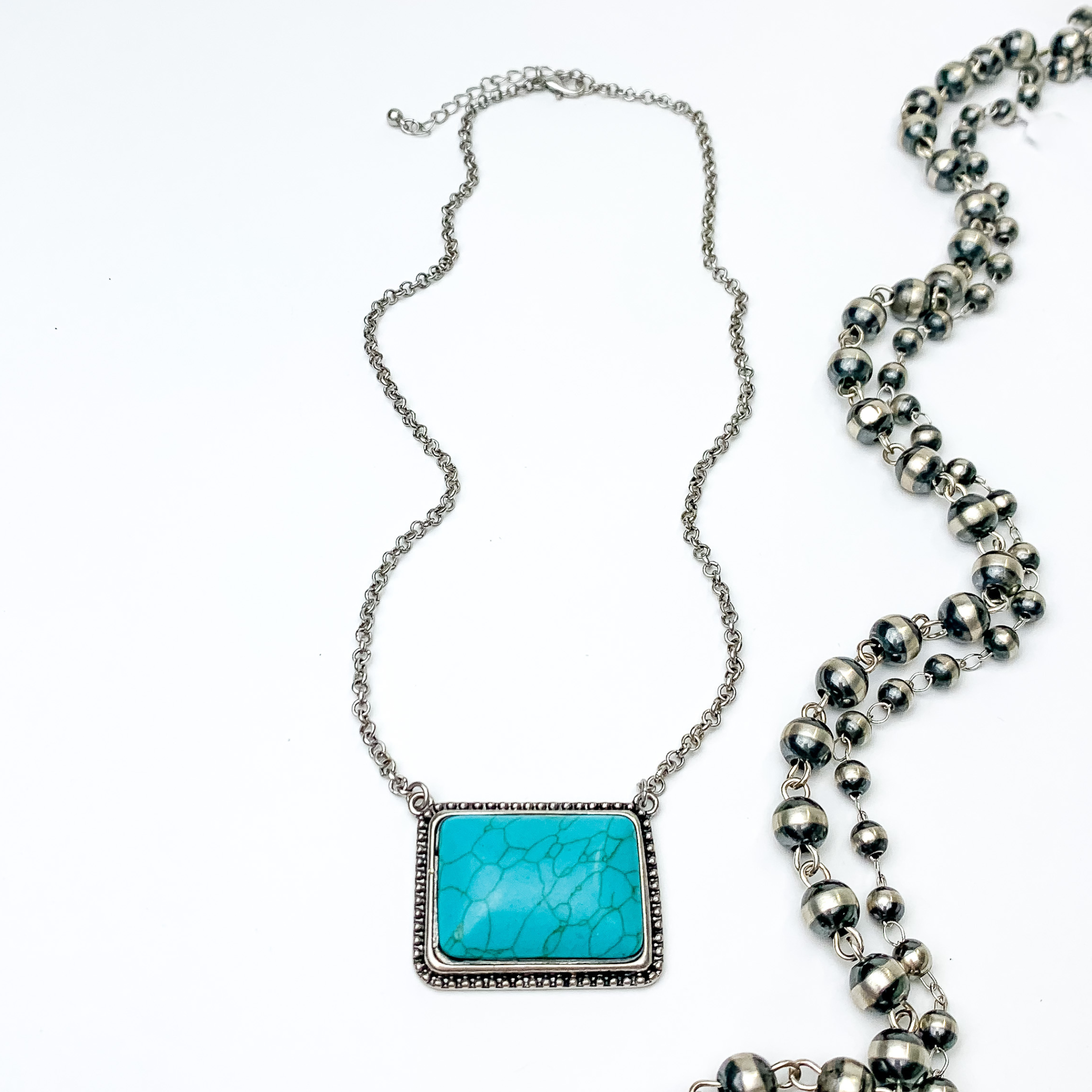 Silver chain necklace with a large, turquoise rectangle pendant with a silver outline. This necklace is pictured on a white background with silver beads on the right side.