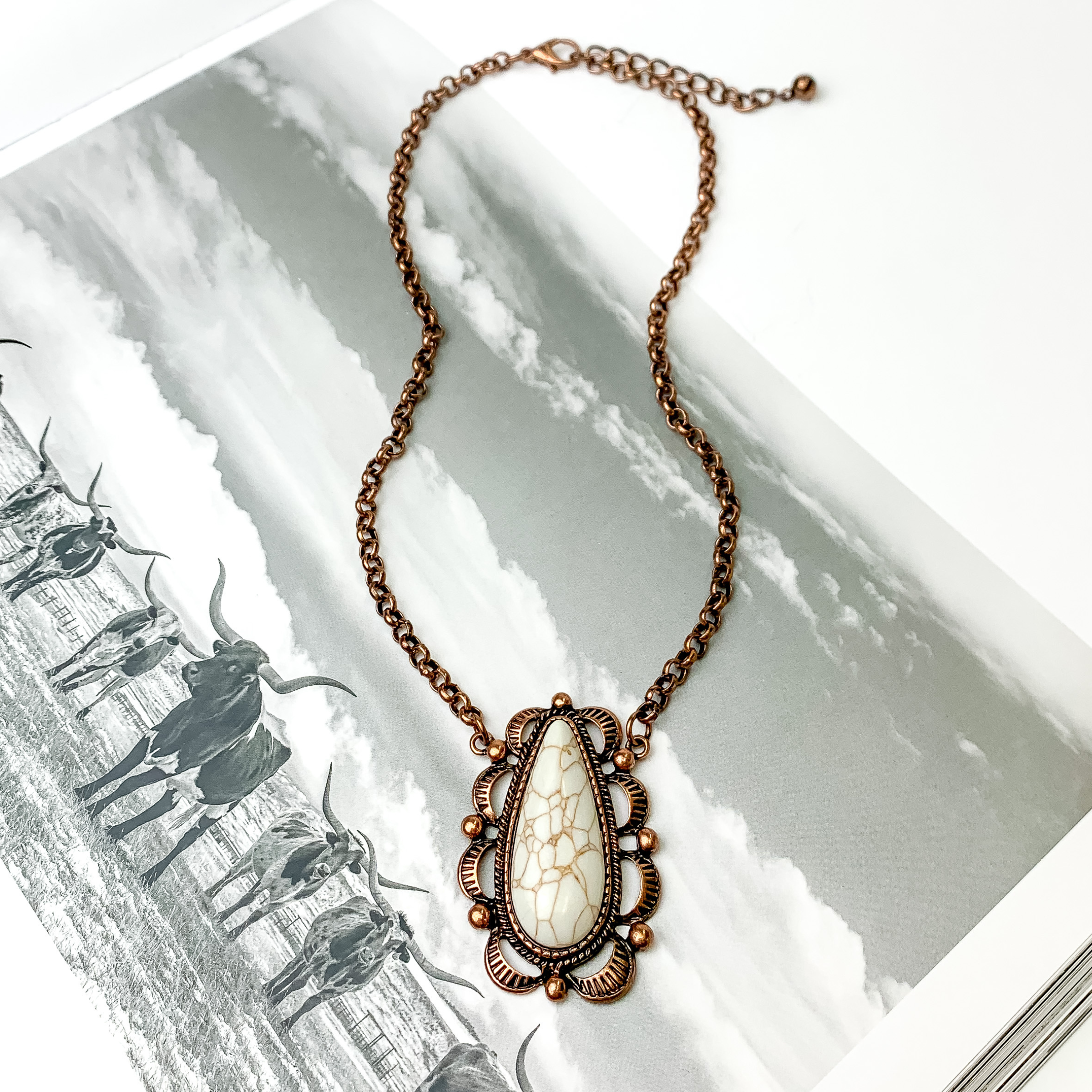 Copper chain necklace with ivory, teardrop stone. The stone also has a detailed copper outline. This necklace is pictured on an open black and white western picture book.