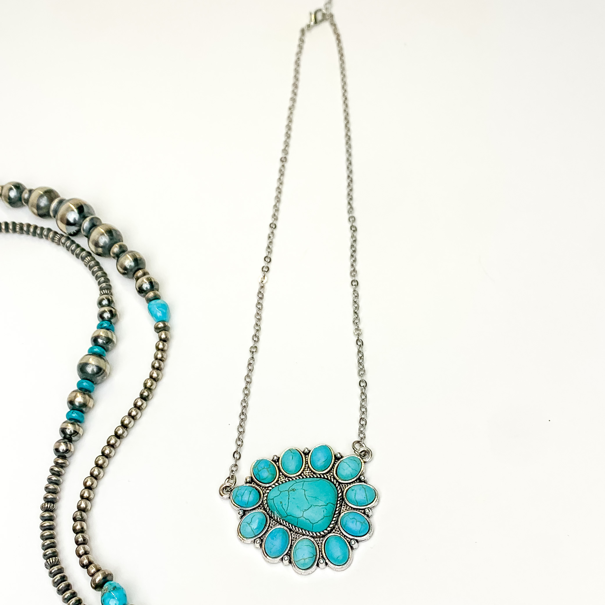 Silver chain necklace with triangular cluster pendant. This pendant is made up of turquoise stones. This necklace is pictured on an white background with silver and turquoise beads on the left side of the picture.