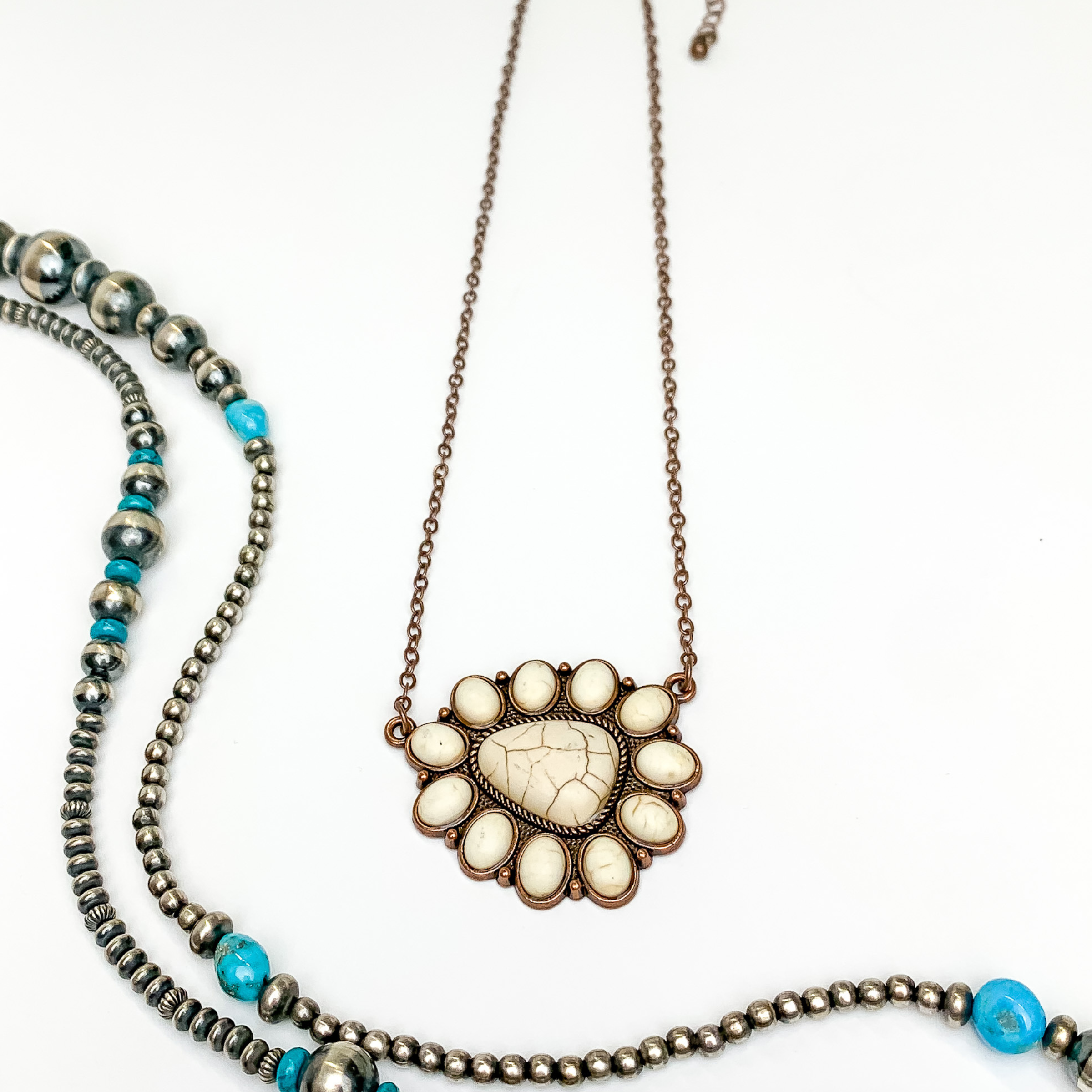 Copper chain necklace with triangular cluster pendant. This pendant is made up of ivory stones. This necklace is pictured on an white background with silver and turquoise beads on the left side of the picture.