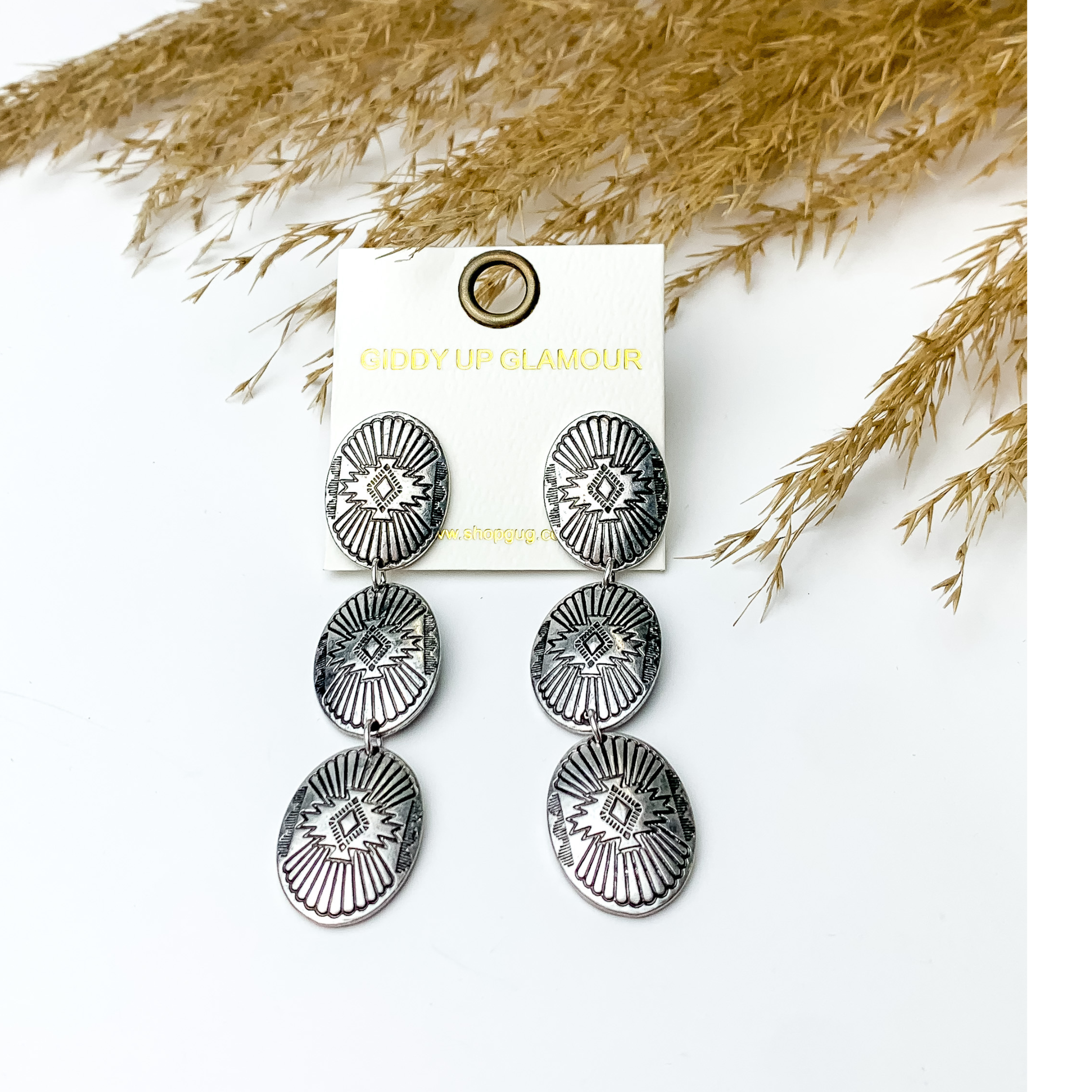 western design concho drop earrings in Silver tone pictured with pampas grass, on a white background. 