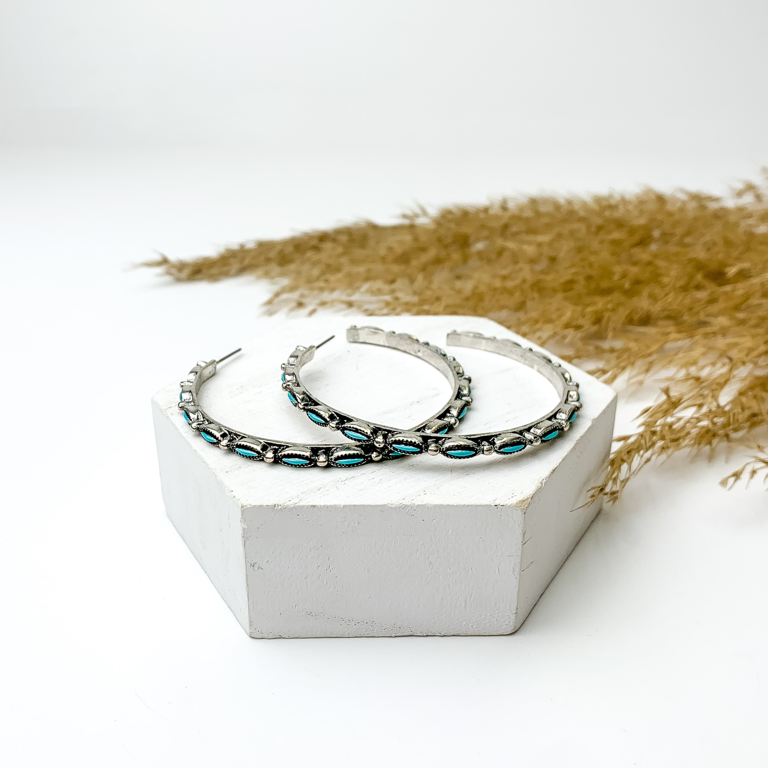 Large silver tone and turquoise hoop earrings, pictured with pampas grass on a white background. 