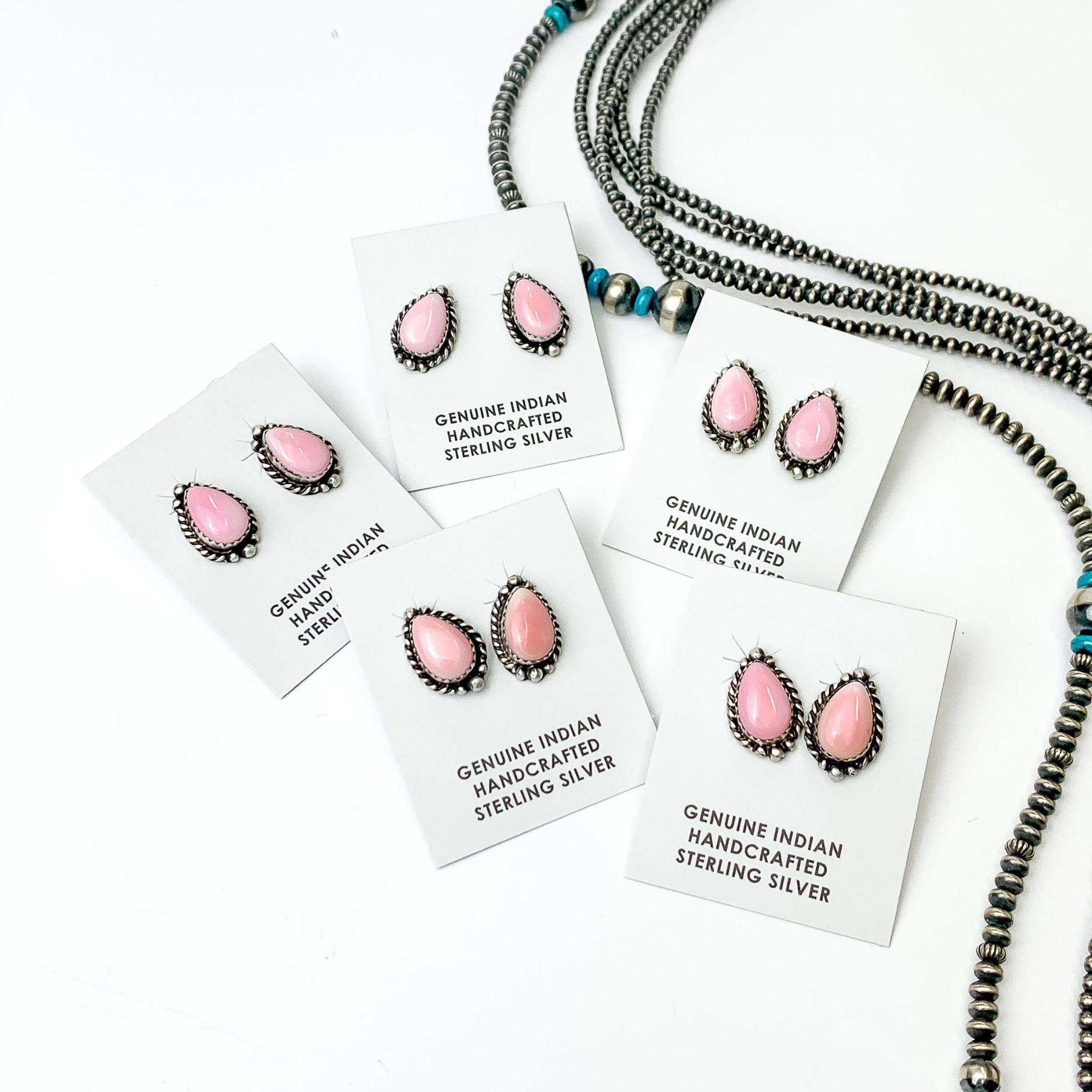 Pictured are five pairs of pink, teardrop stud earrings with silver outline. These earrings are pictured on a white background with silver beads on the right side of the picture. 