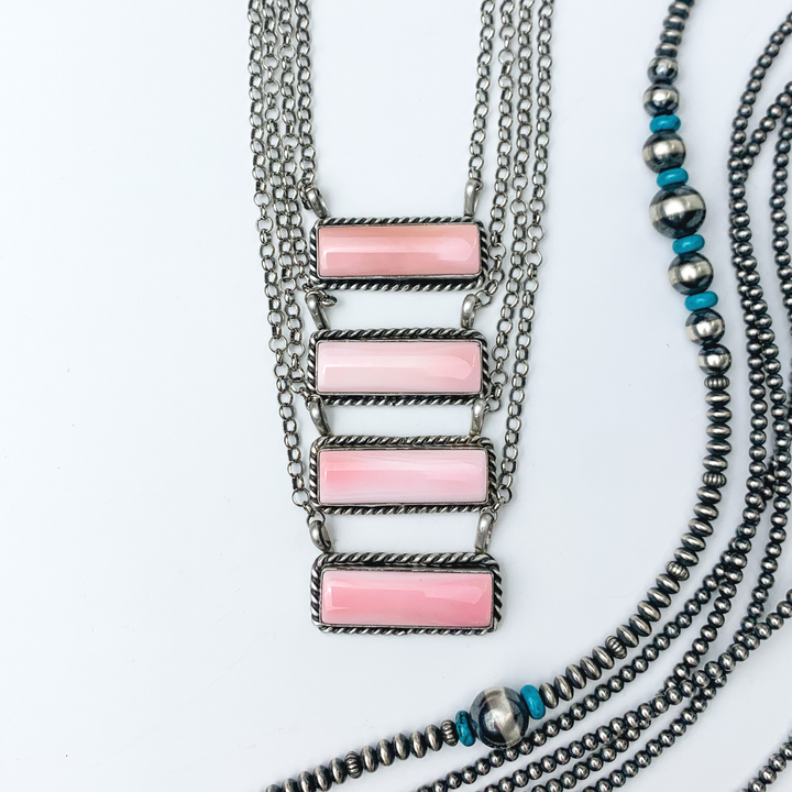Pictured are four pink conch rectangle bar necklaces. These necklaces include a silver outline and silver chain necklace. These necklaces are pictured on a white background with silver beads on the right side of the picture. 