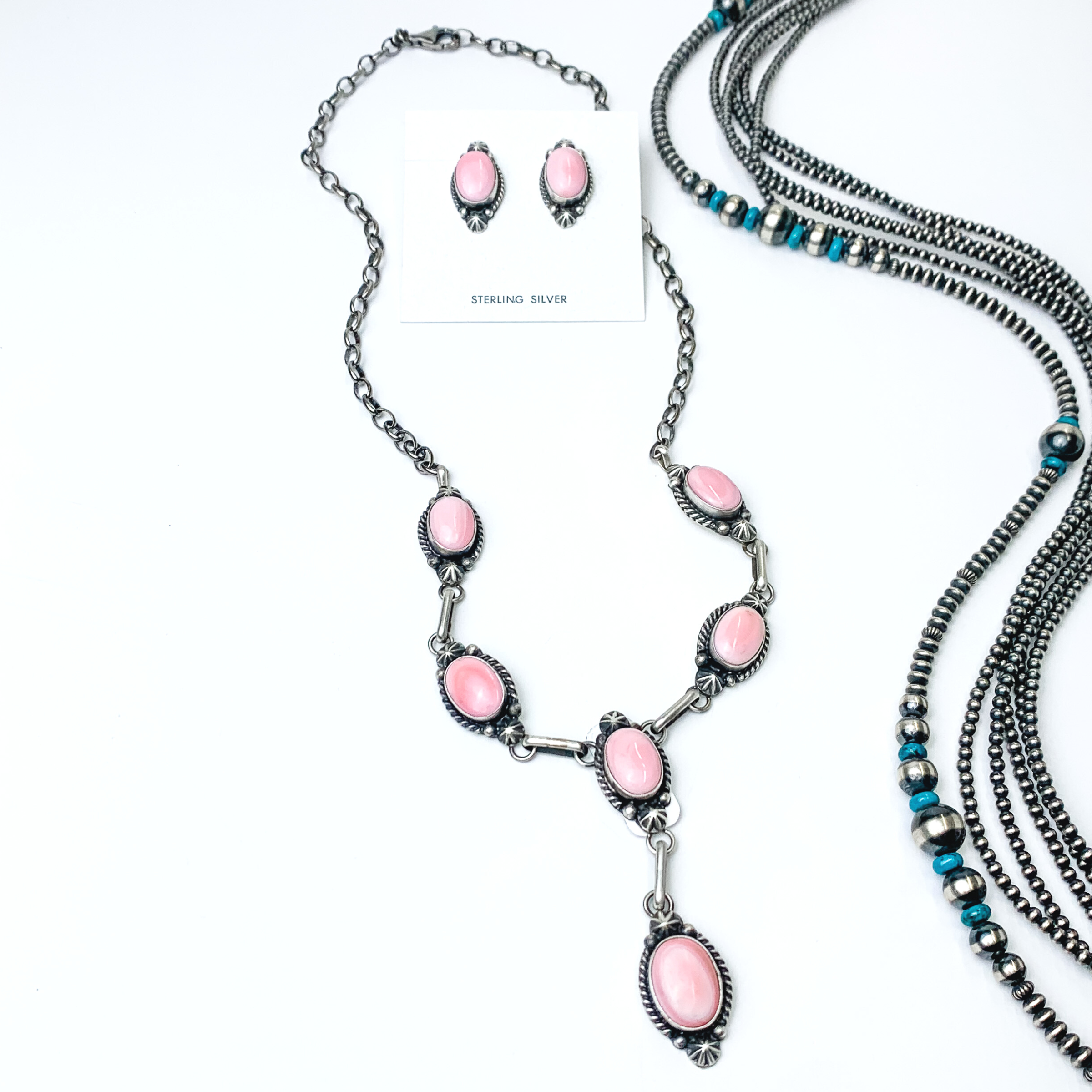Pictured is a pink stone lariat necklace that includes six stones. There is also a pair of pink oval stones. This necklace set is pictured on a white background with silver beads to the right of the necklace. 