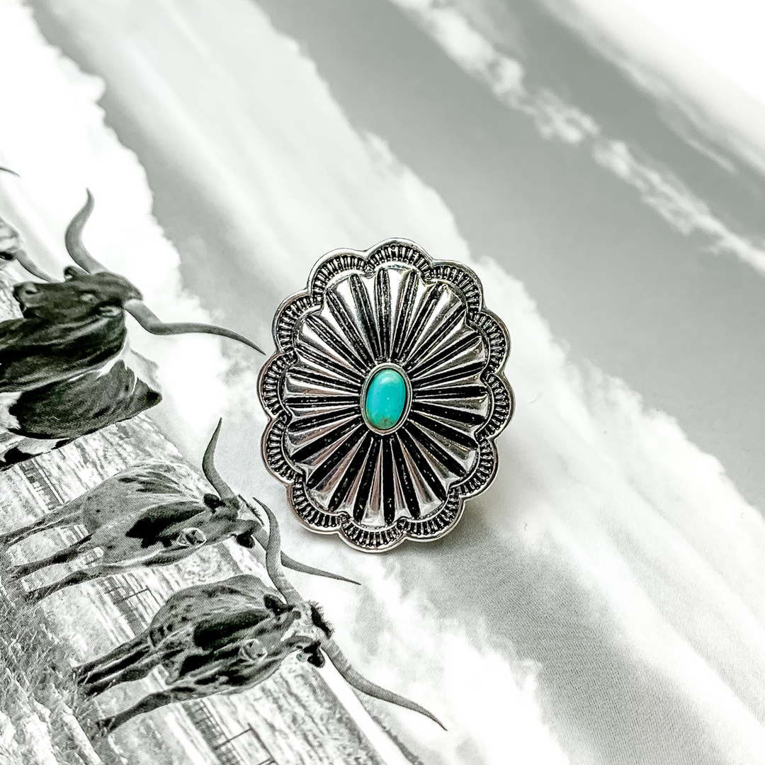 Silver, oval concho ring with a small turquoise center stone. This ring is pictured on a black and white picture. 