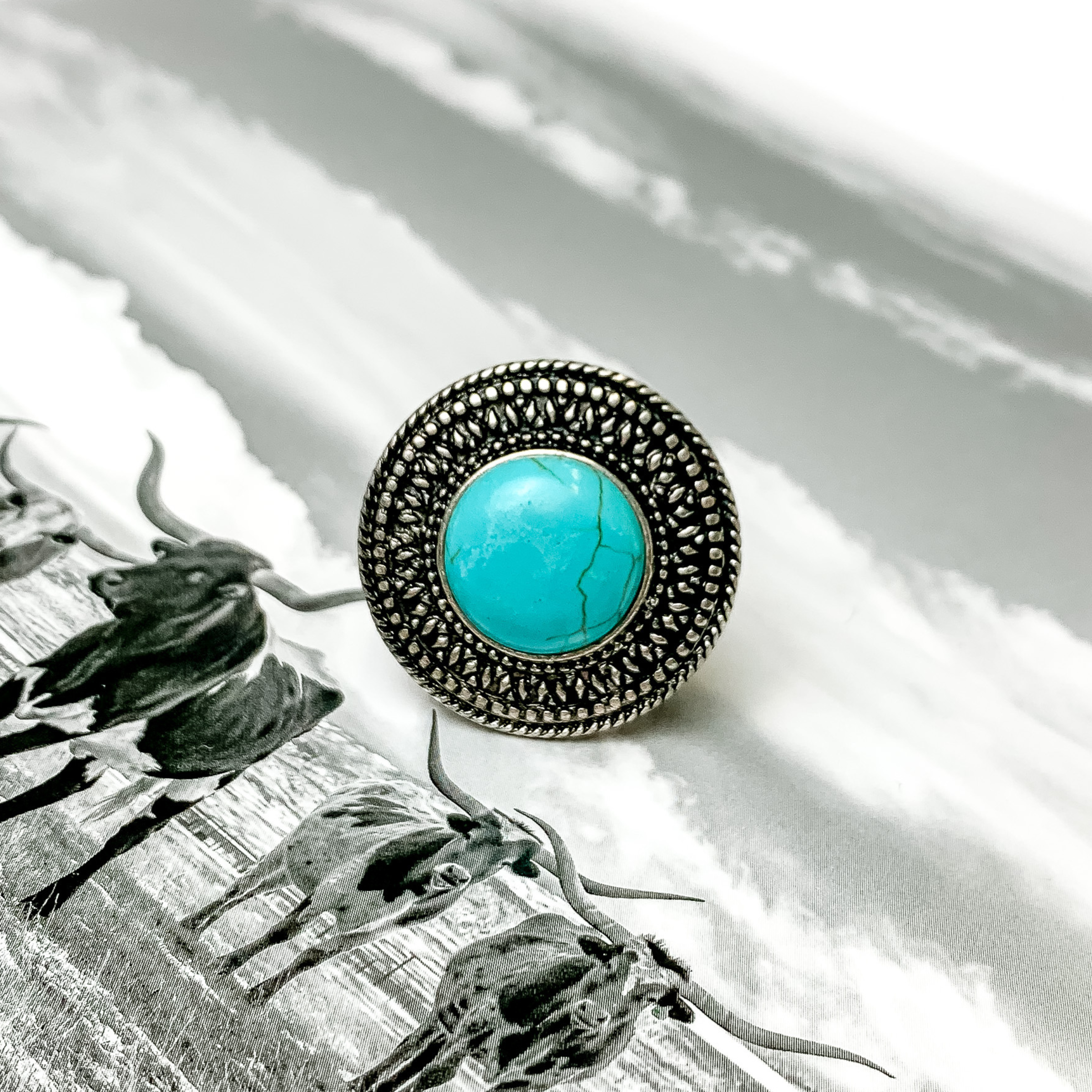 Silver, circle ring with a turquoise center stone. This ring is pictured on a black and white picture. 