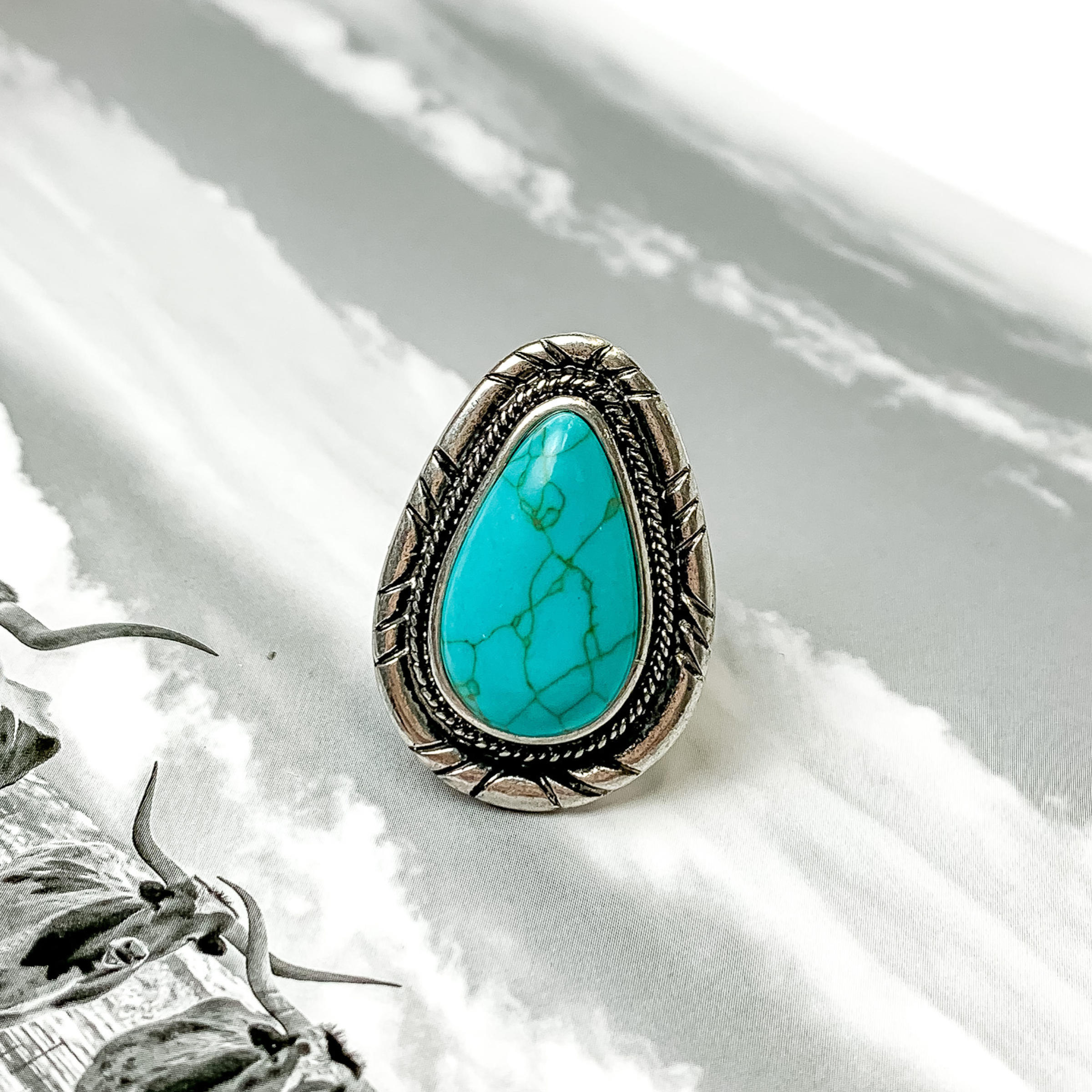 Silver, teardrop ring with a turquoise center stone. This ring is pictured on a black and white picture. 
