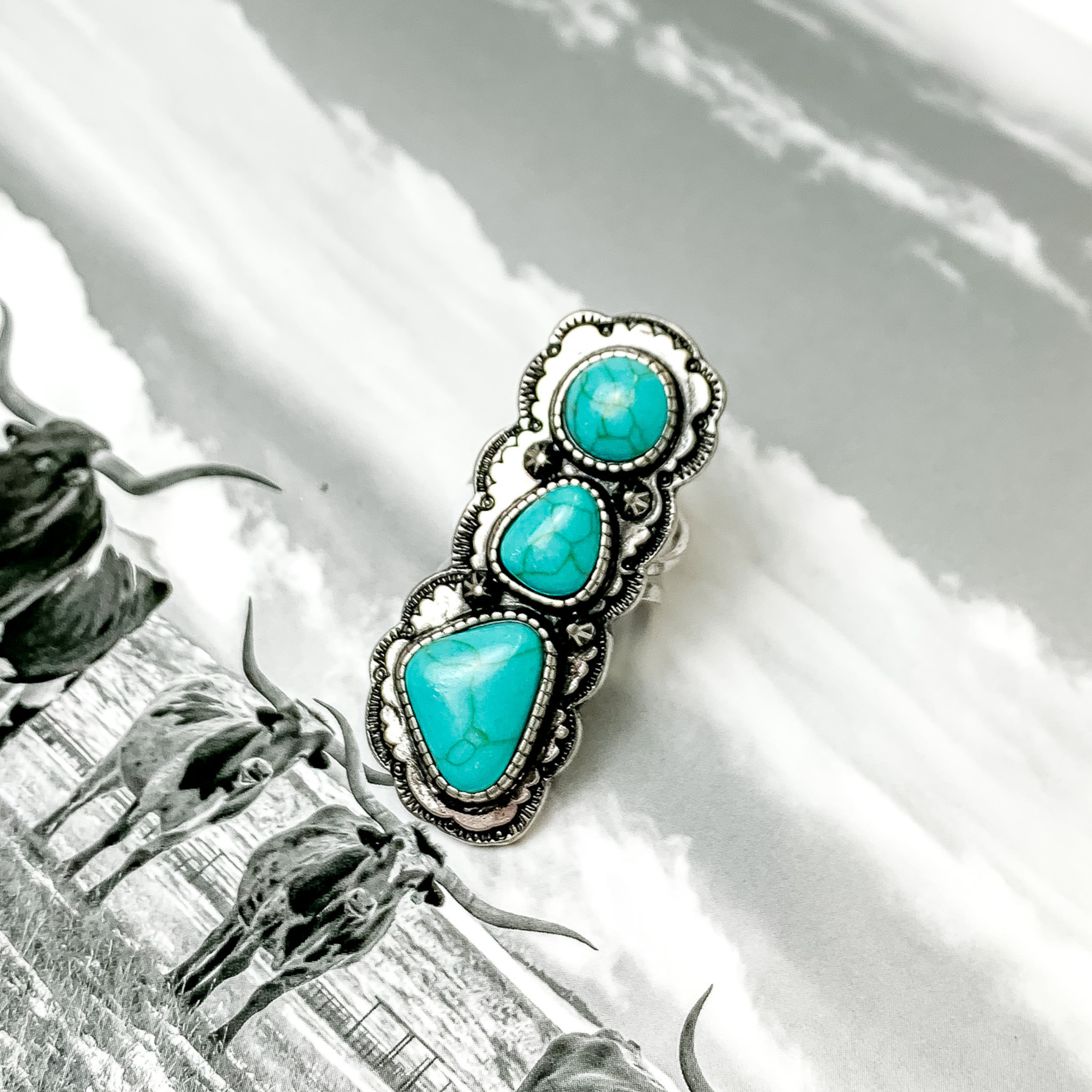Silver ring with three irregular shaped turquoise stones. This ring is pictured on a black and white picture. 