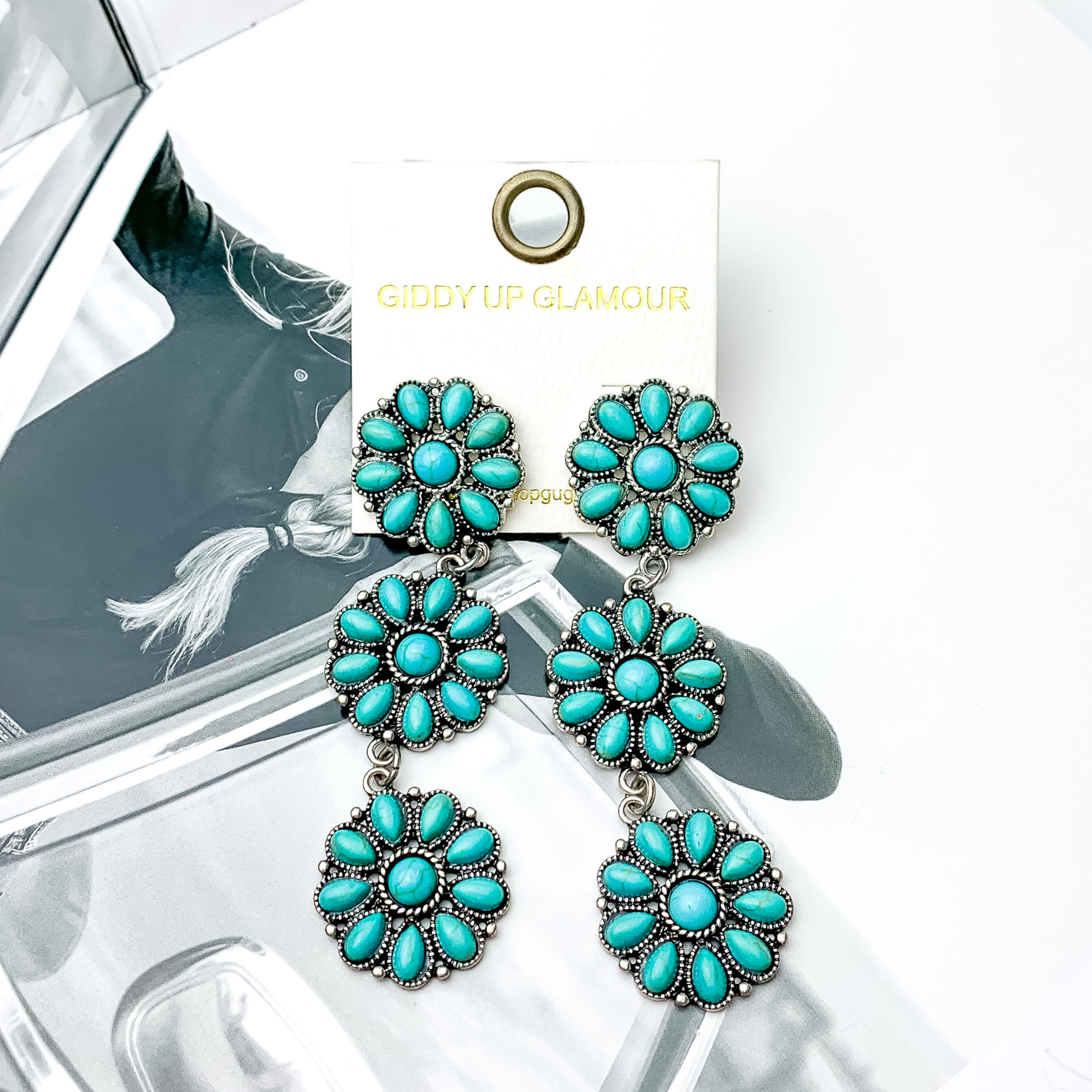 Three turquoise flower cluster drop earrings. These earrings are pictured on a black and white picture. 