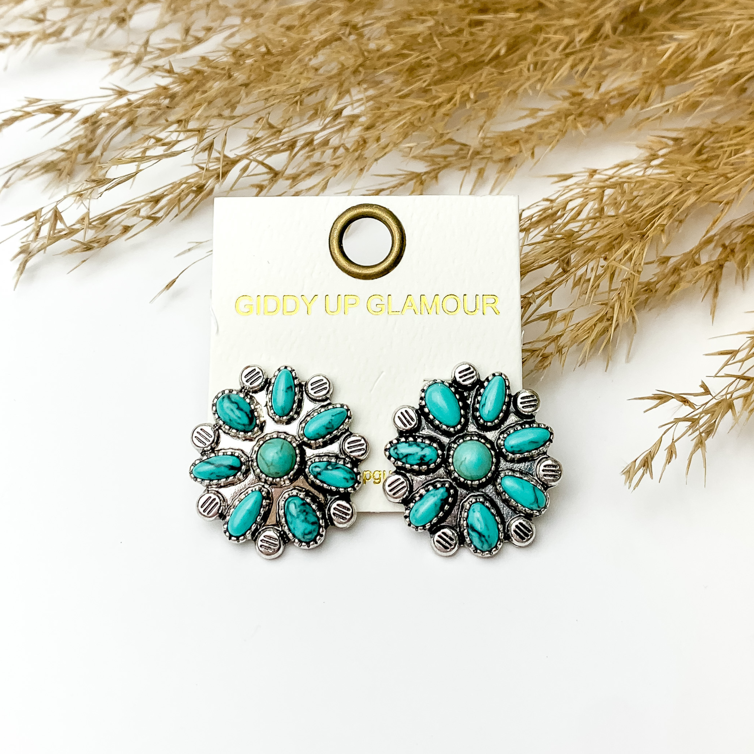 Three turquoise flower cluster stud earrings. These earrings are pictured on a white background in front of tan pompous grass. 