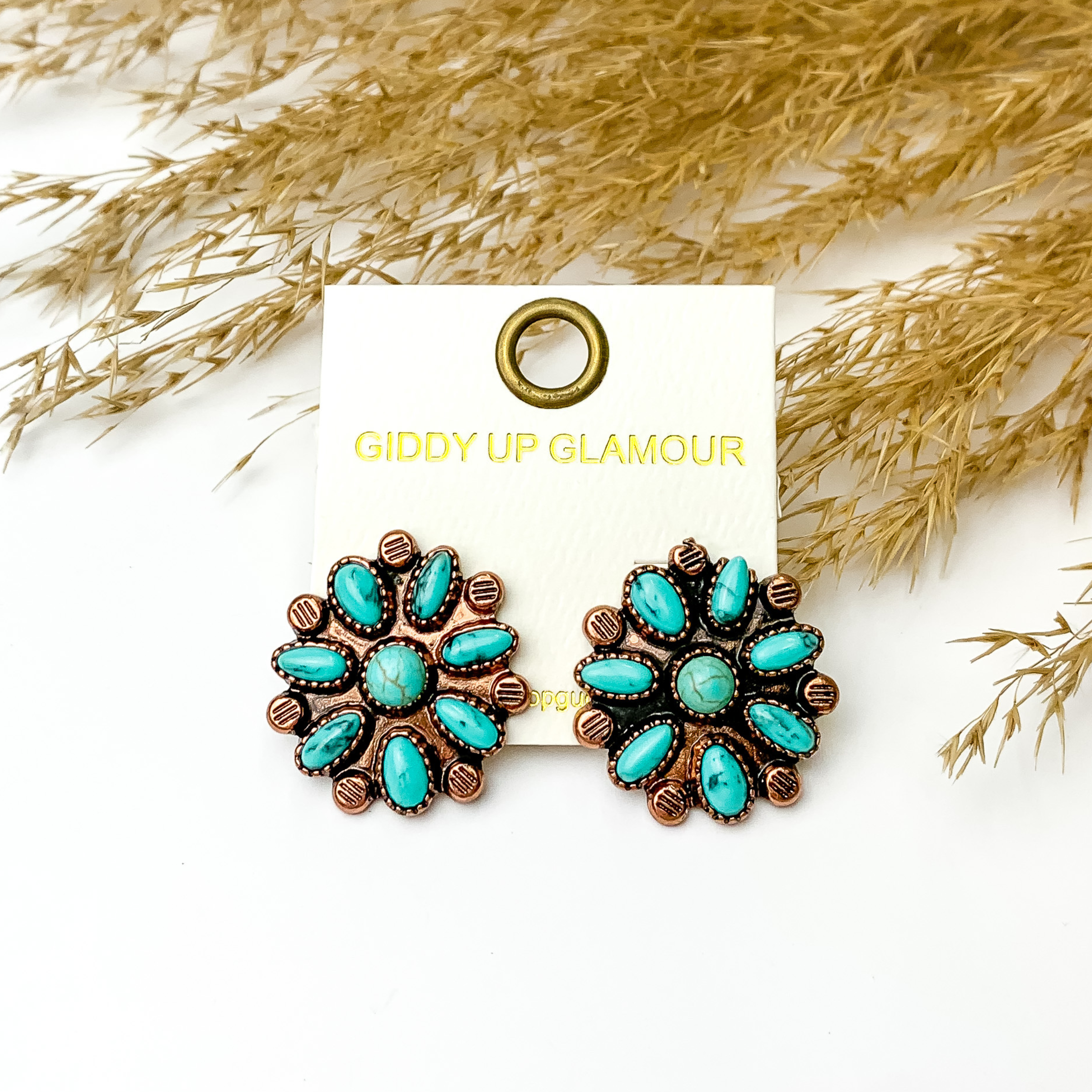 Three turquoise flower cluster stud earrings in copper. These earrings are pictured on a white background in front of tan pompous grass. 