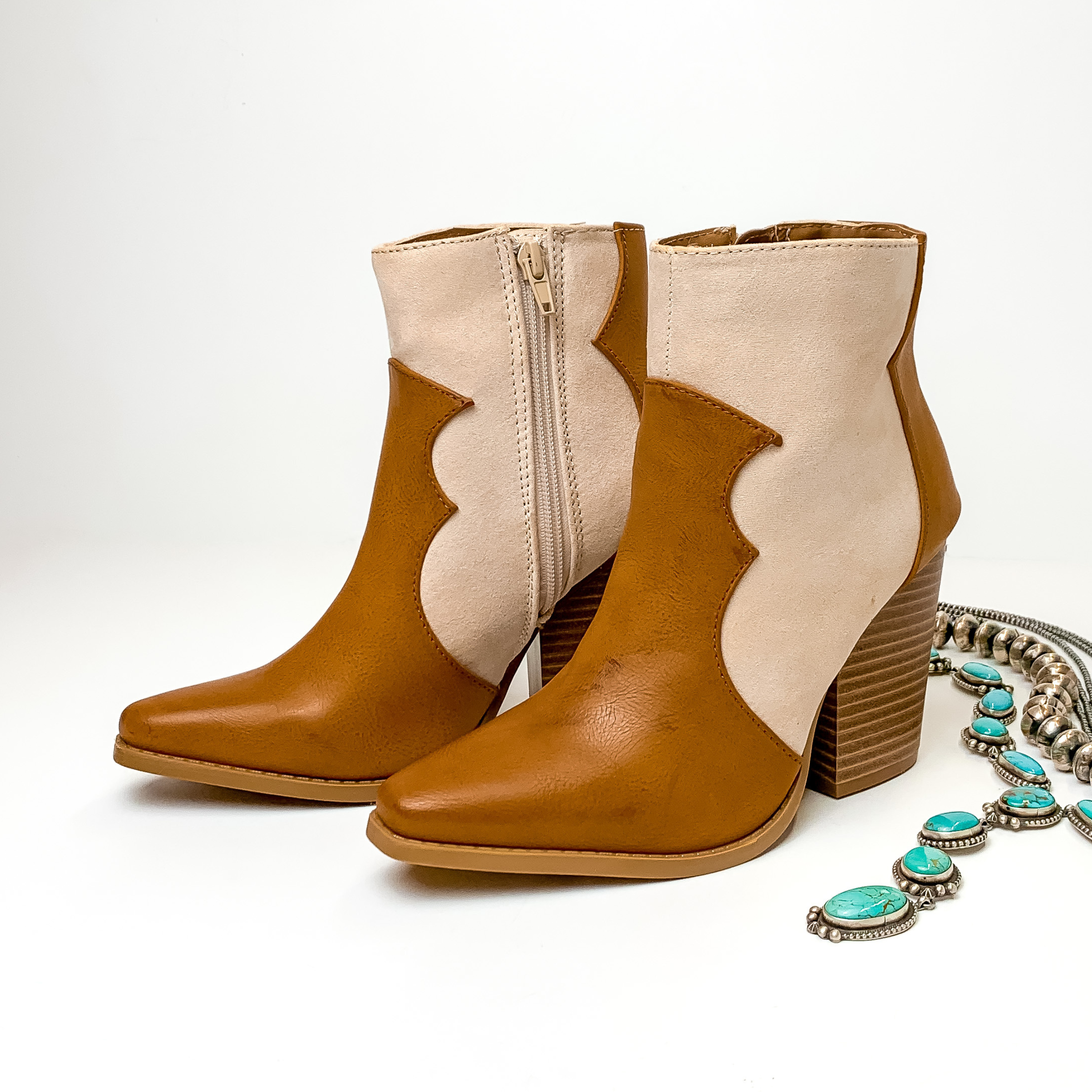 Two tone heeled booties with ivory and camel burnishing. These boots are pictured on a white background with jewelry laying to the right of the boots. 
