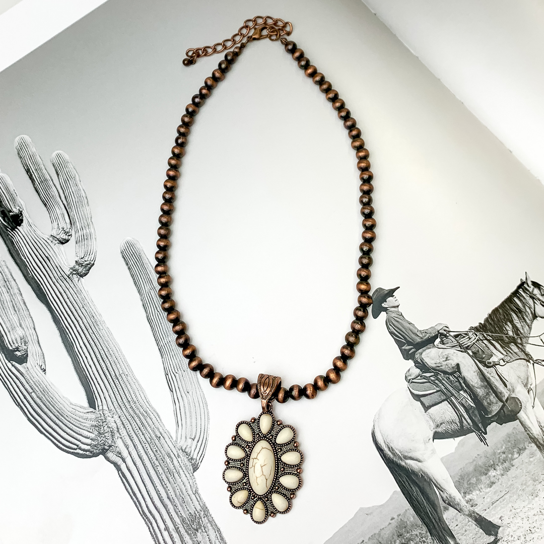 Copper beaded necklace with an oval pendant. This pendant is copper with an ivory stone design. This necklace is pictured on a black and white picture. 