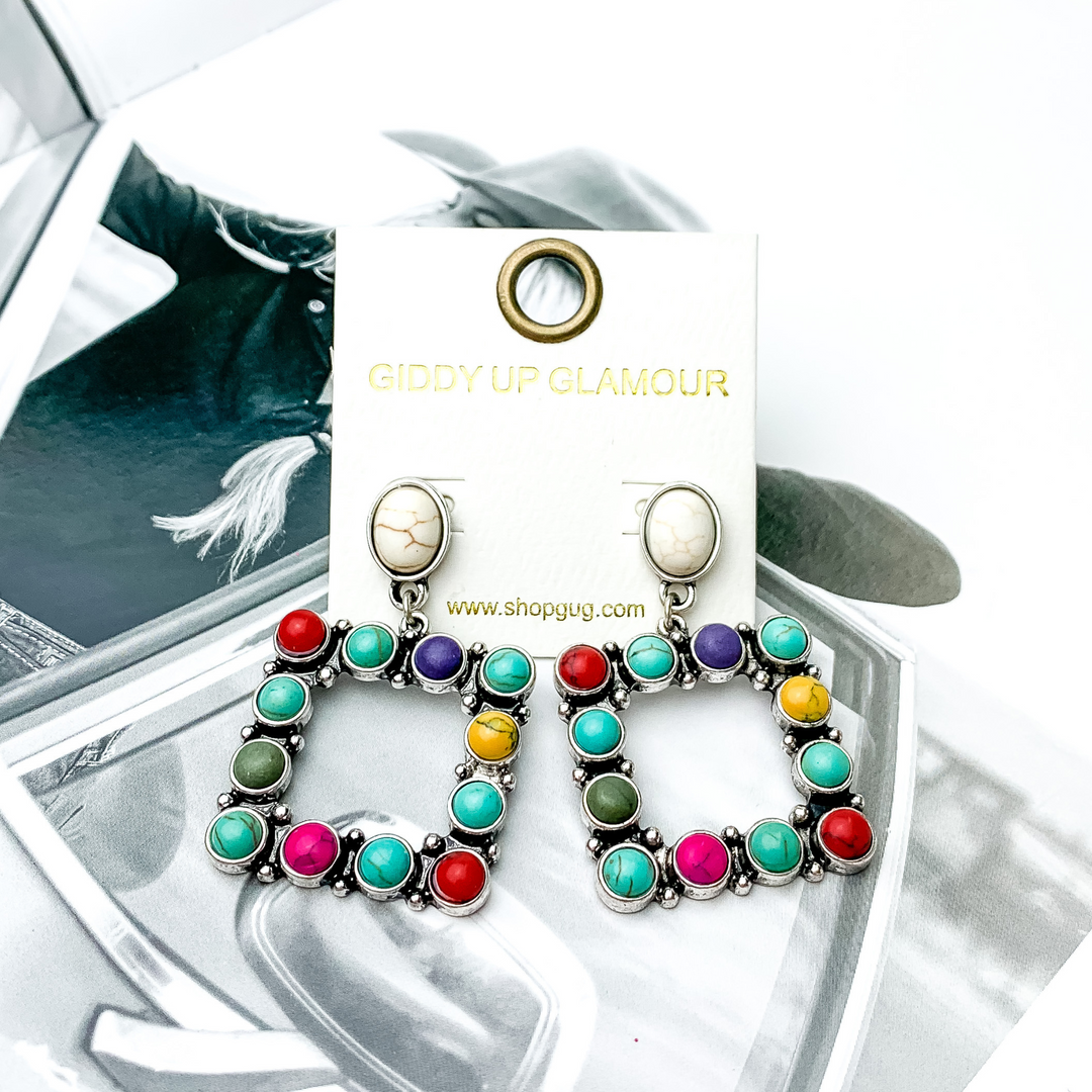 Open square drop earrings with ivory studs. These earrings include pink, turquoise, green, yellow, pink, red, and pruple stones. These earrings are pictured on a black and white picture. 