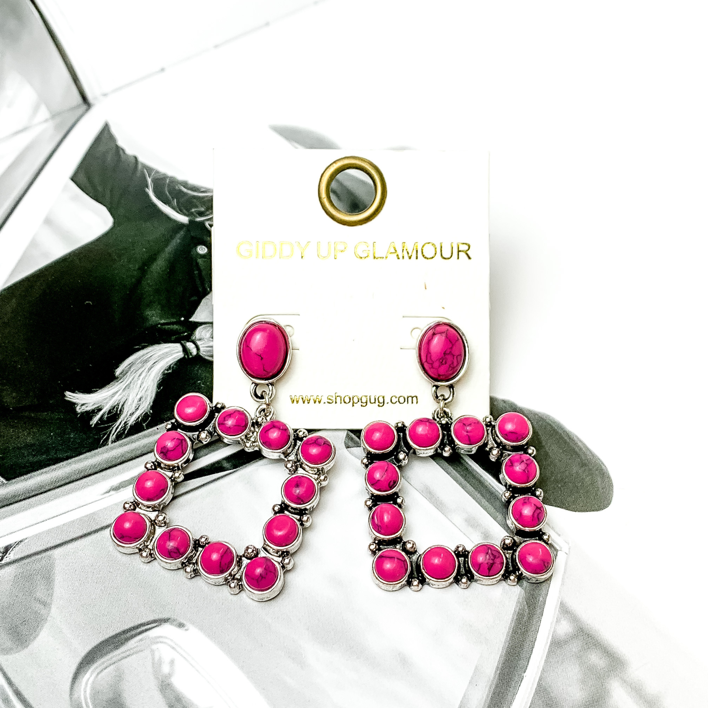 Open square drop earrings with fuchsia pink stones. These earrings are pictured on a black and white picture. 