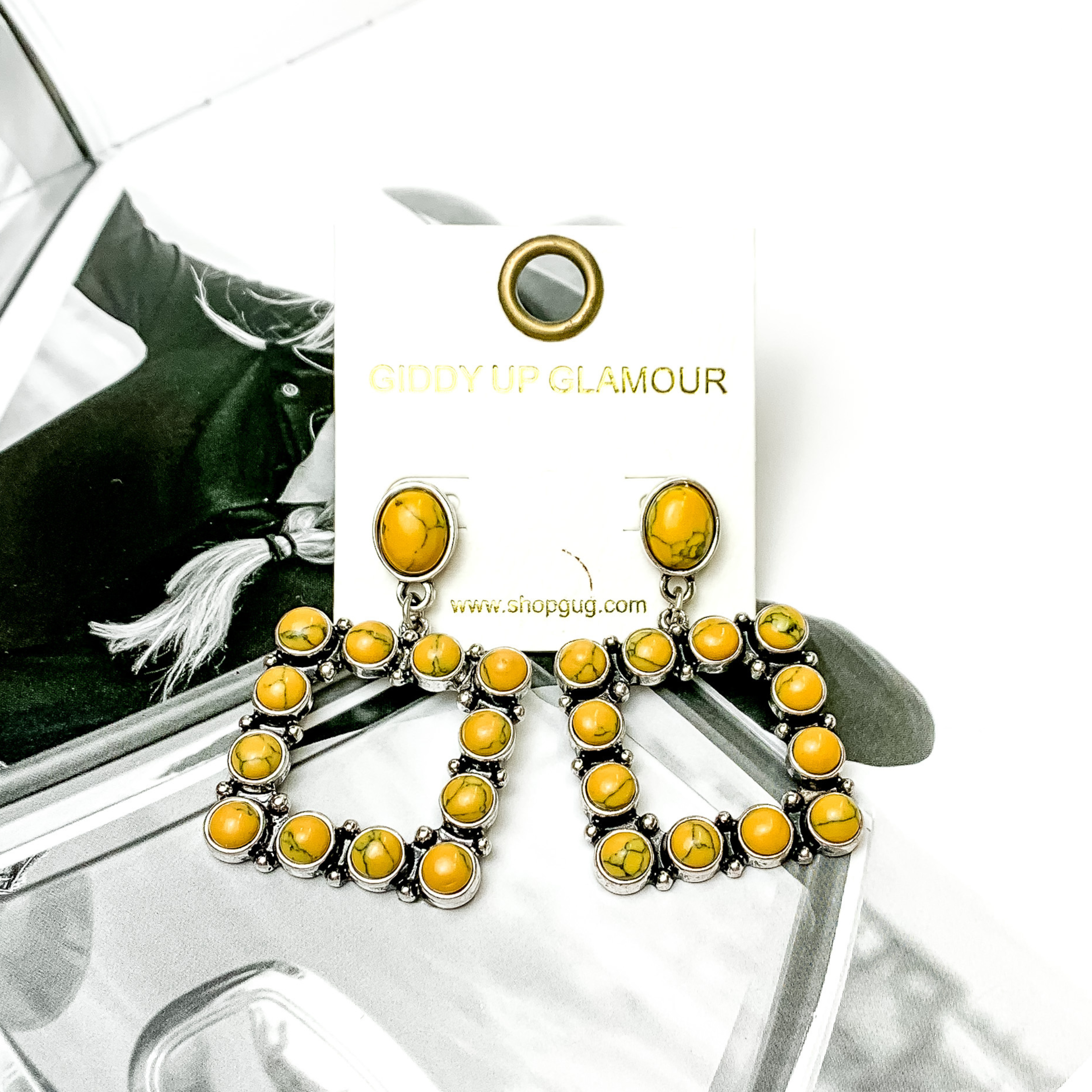 Open square drop earrings with mustard yellow stones. These earrings are pictured on a black and white picture. 