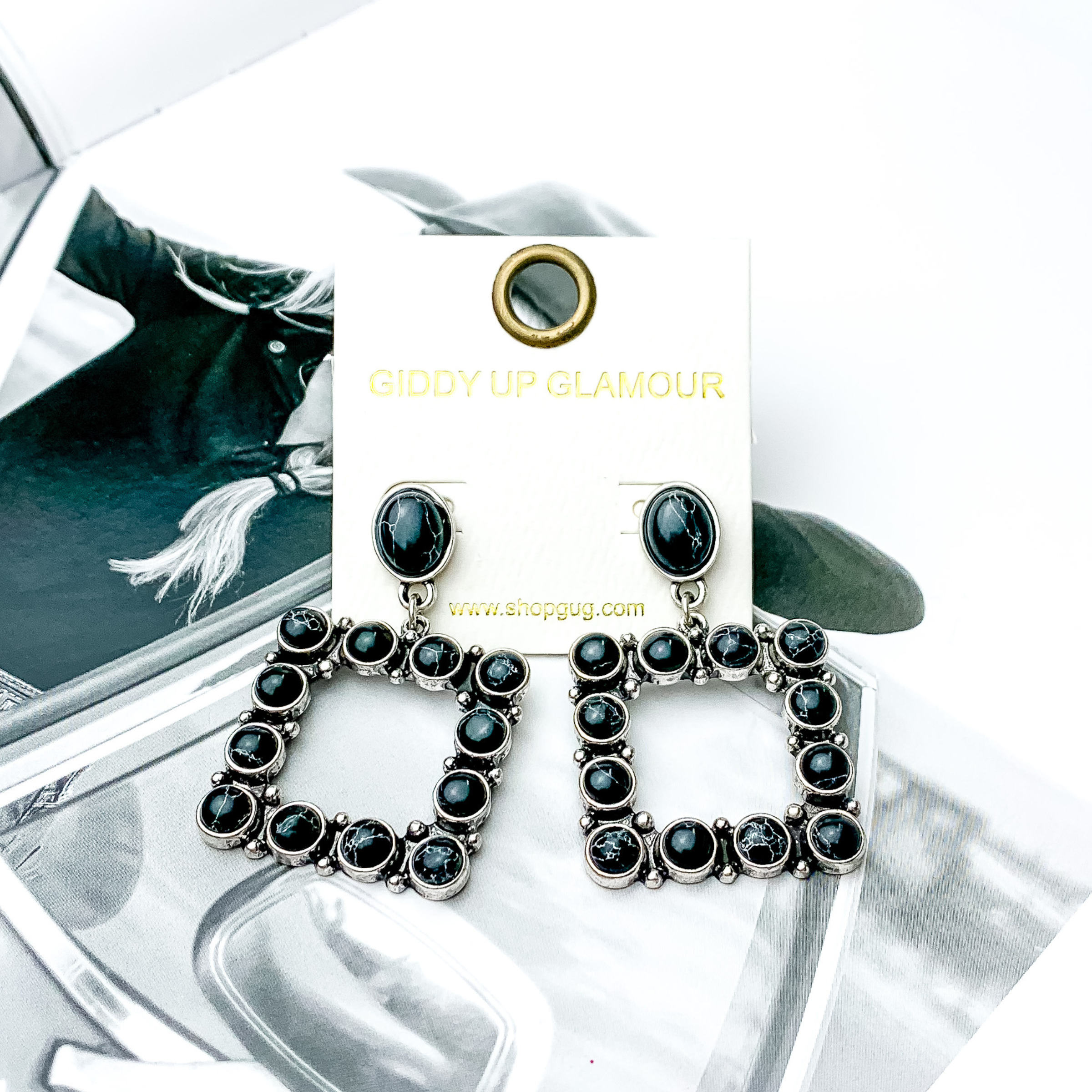 Open square drop earrings with black stones. These earrings are pictured on a black and white picture. 