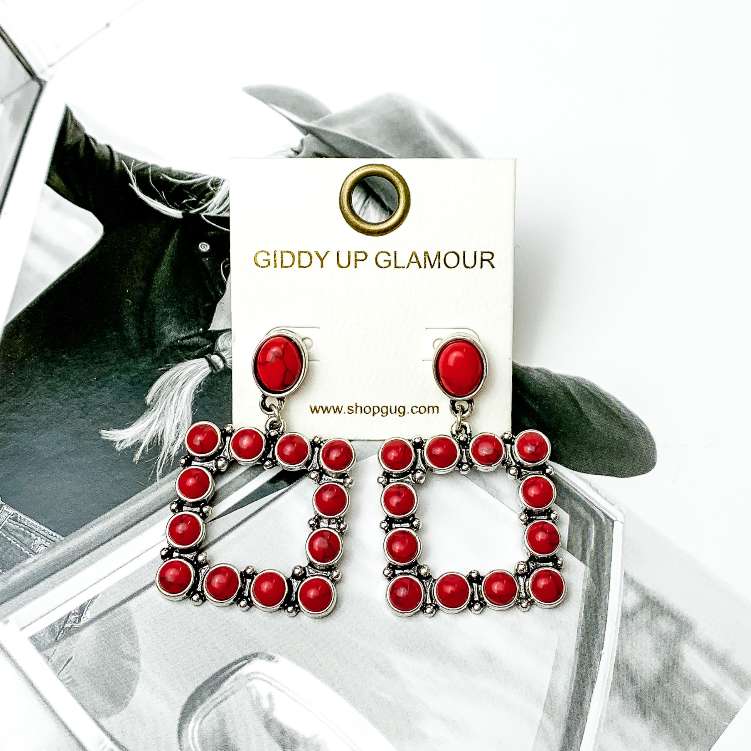Open square drop earrings with red stones. These earrings are pictured on a black and white picture. 