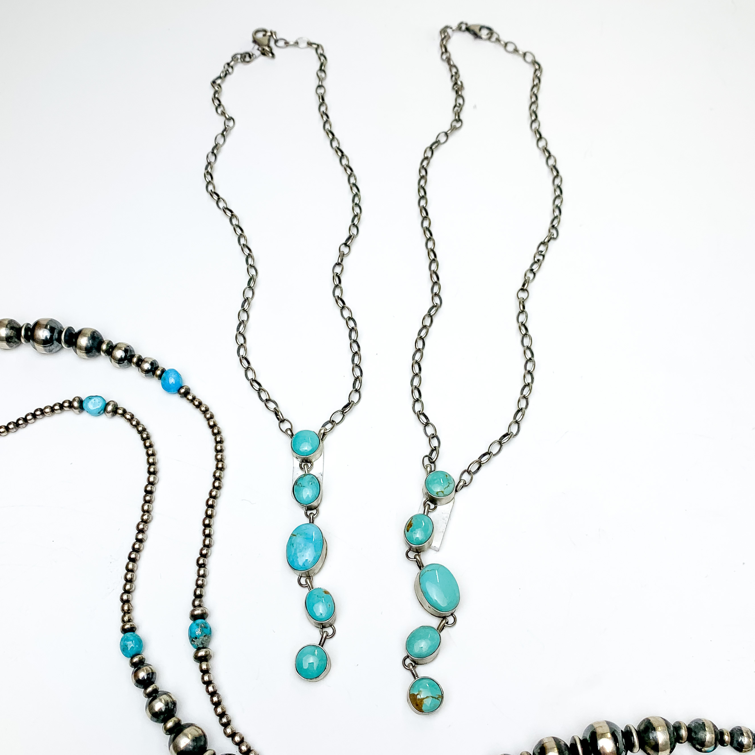 Two silver chain necklaces with a lariat stone pendant. The pendant ias five, oval turquoise stones. These necklaces are pictured on a white background with silver beads at the bottom of the picture.  