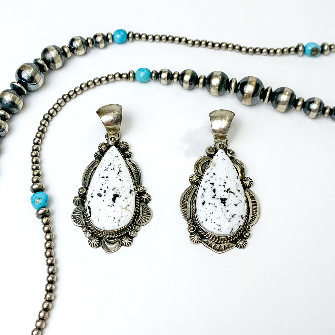 Two silver, teardrop pendants with white buffalo teardrop stone. These pendants are pictured on a white background with silver beads at the top of the picture.  