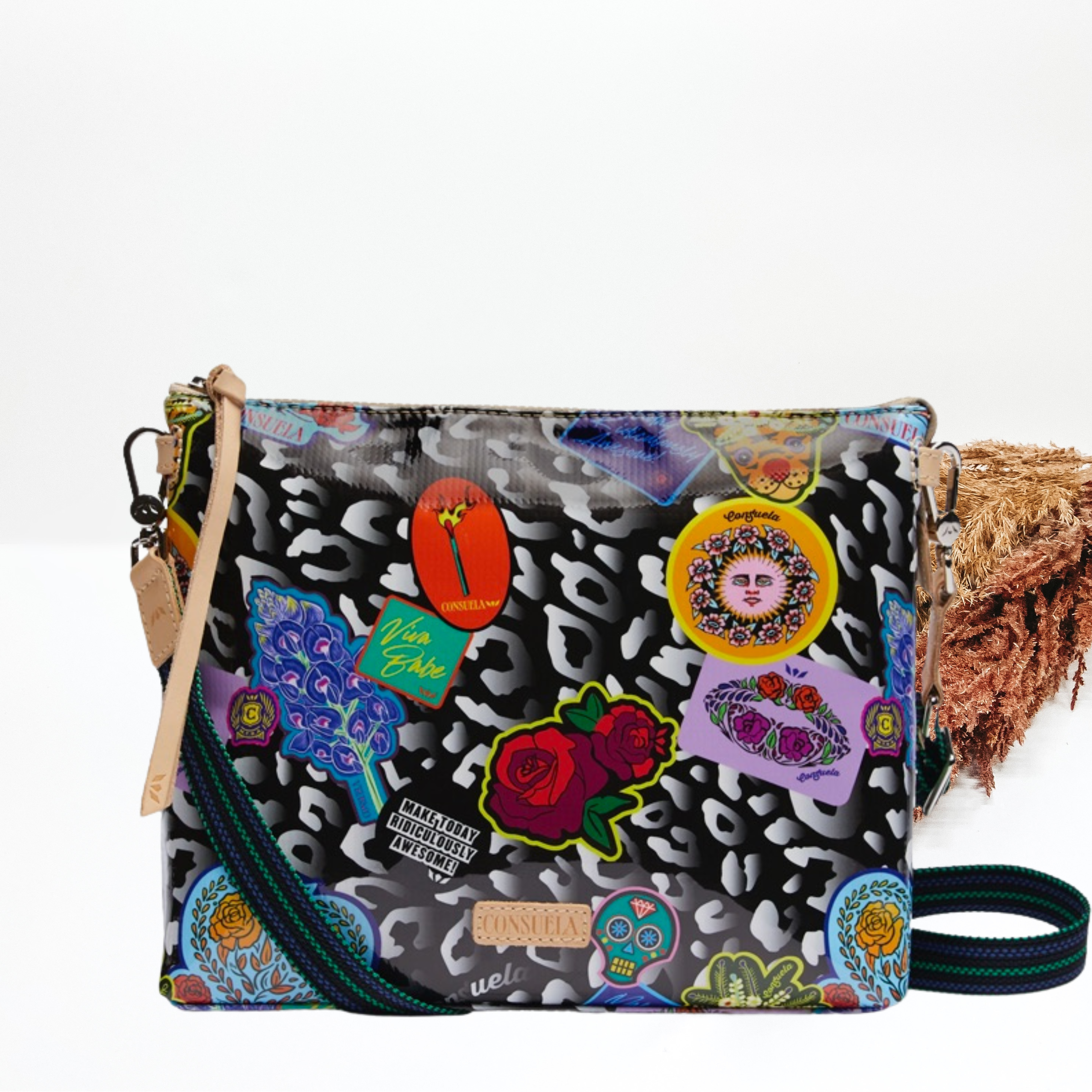 Pictured is a crossbody purse with a mostly black purse with a grey leopard print design. This purse also includes random stickers all over the leopard print. This purse is pictured on a white background with pompous grass on the right side of the picture.