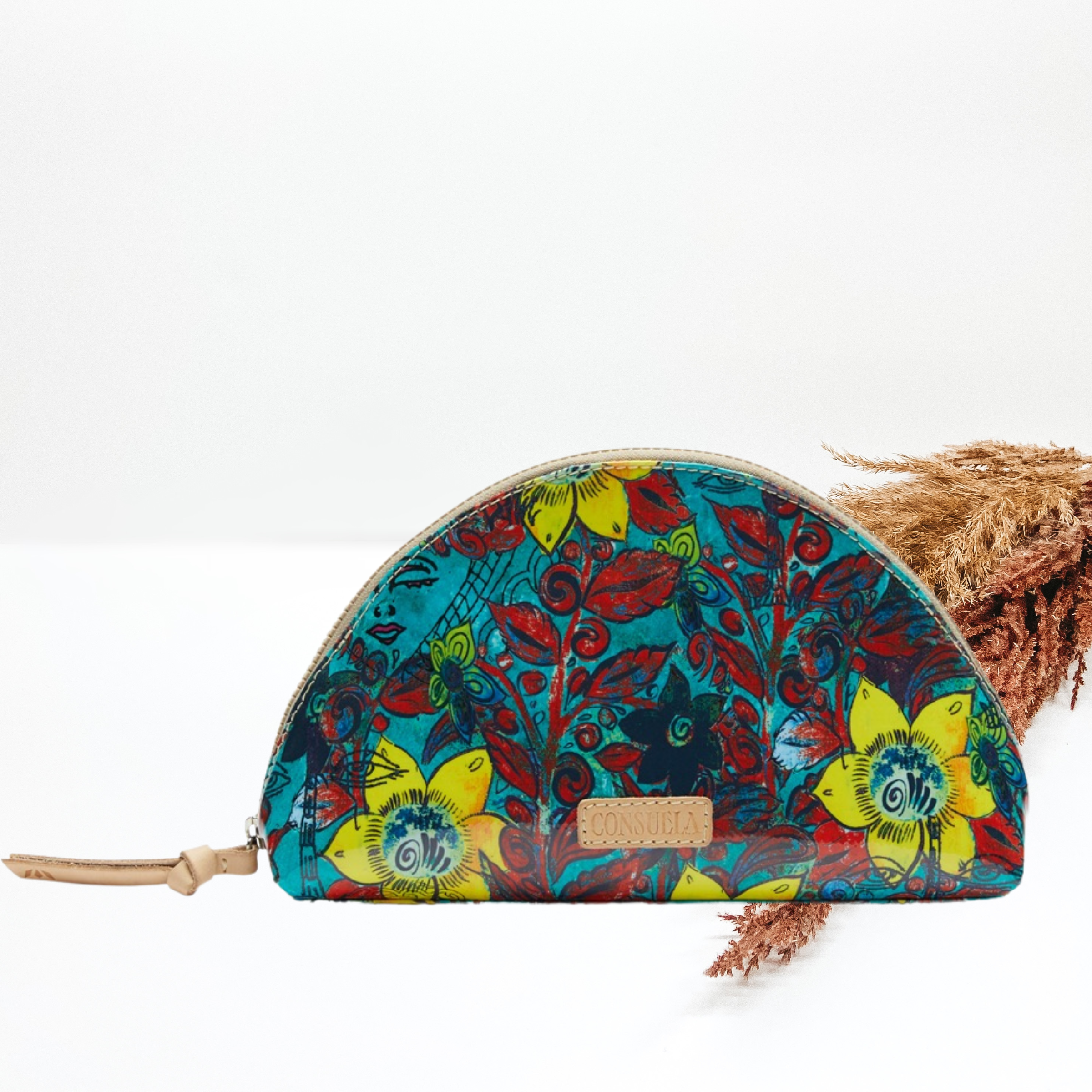Pictured is a dome shaped cosmetic bag. This is a blue bag with a nacy, yellow, and red print design. It also includes a top zipper. This purse is pictured on a white background with pompous grass on the right side of the picture.