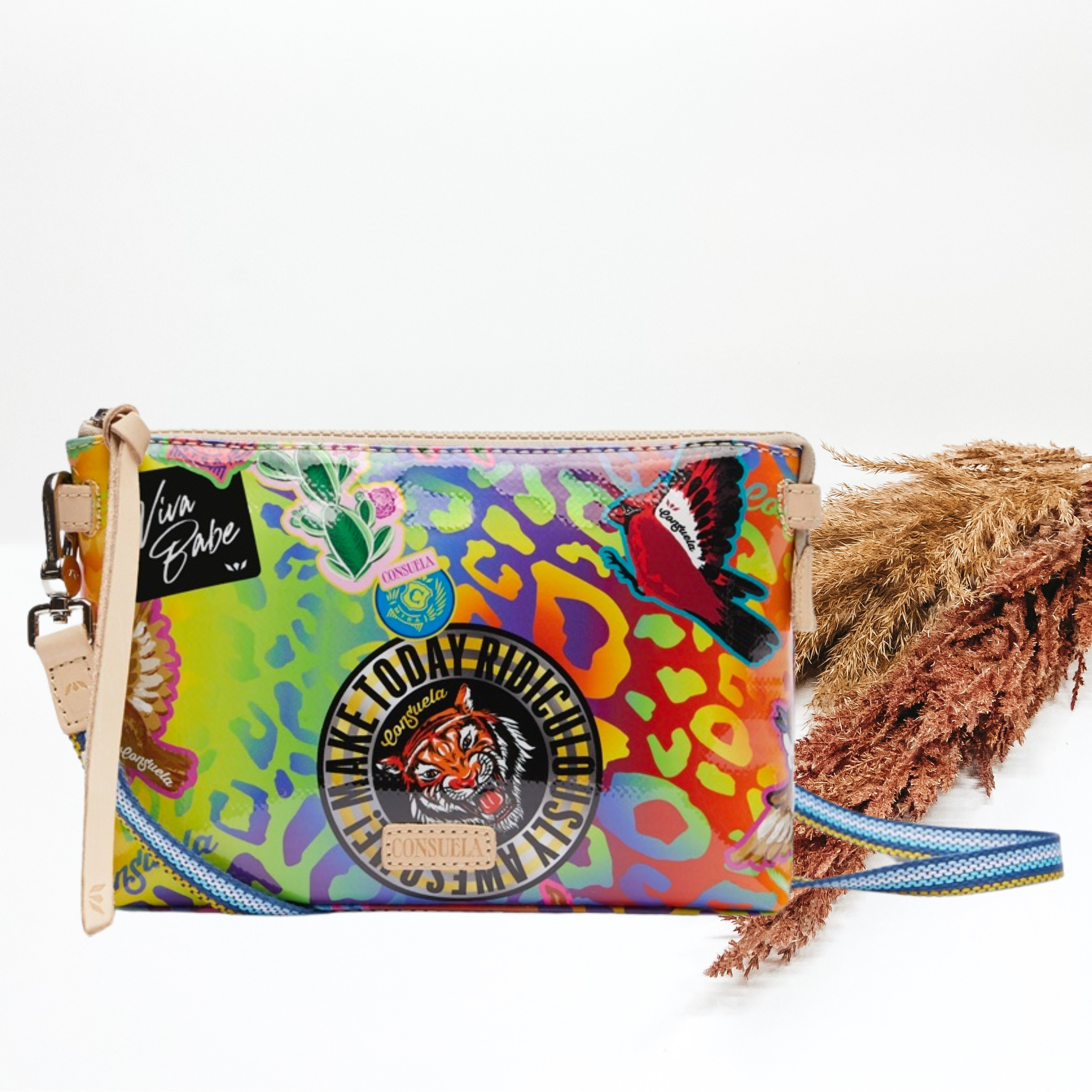 Pictured is a rectangle crossbody purse. This purse has a mostly a multicolored leopard print design. It also includes random sticker patches throughout the bag and a top zipper. This purse is pictured on a white background with pompous grass on the right side of the picture.