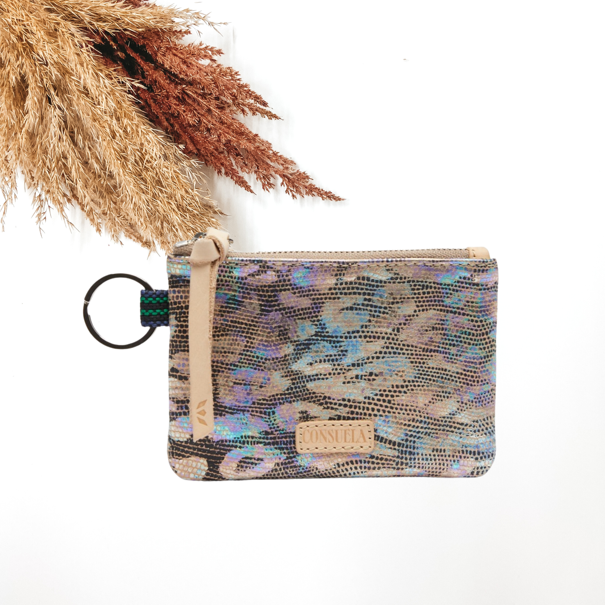 Small, rectangle pouch with a silver key ring on the left side and a light tan zipper pull. This pouch has a iridescent, multicolored leopard print design. This purse is pictured on a white background with tan and brown pompous grass on the right side.
