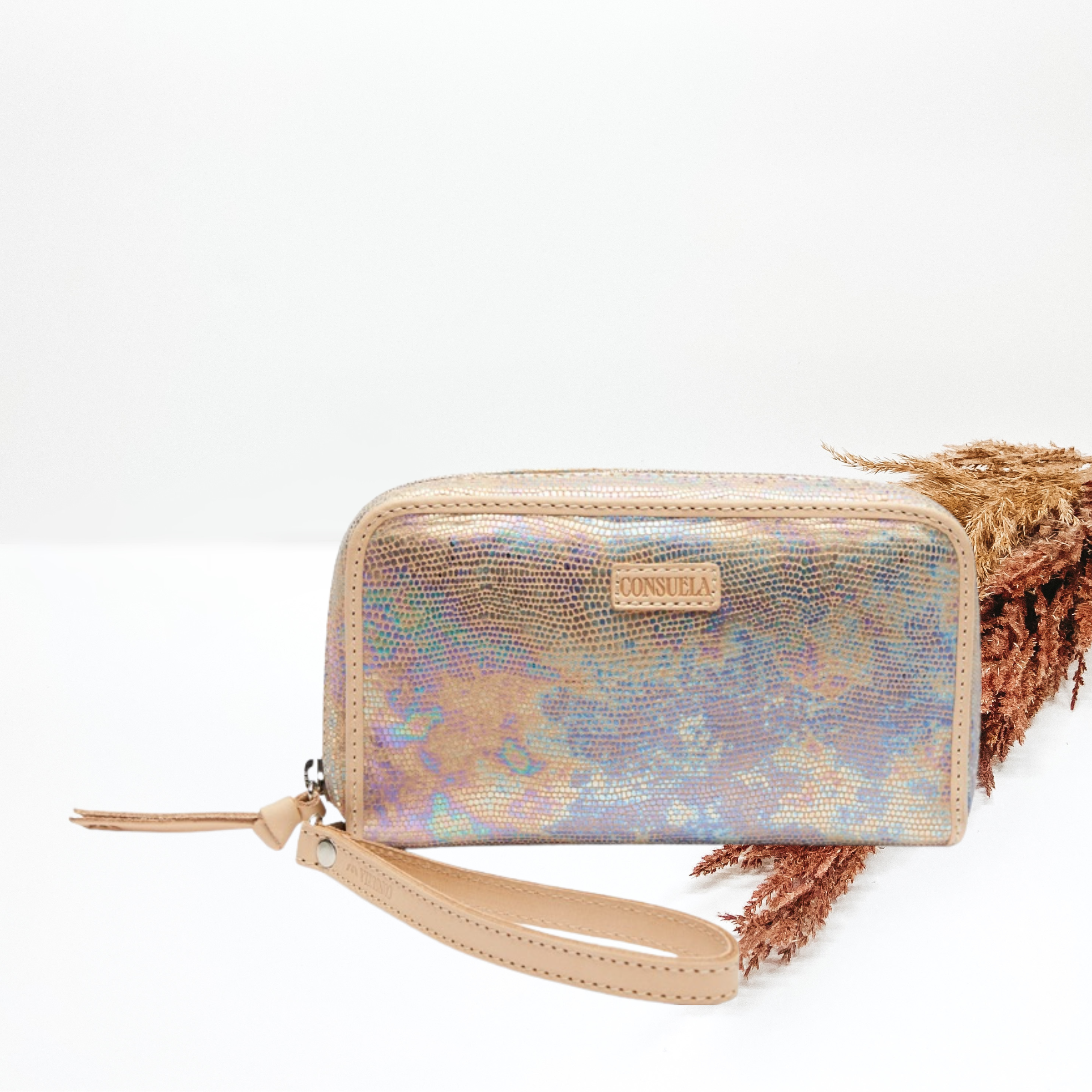 In the middle of the picture is a wristlet wallet in a iridescent color. Background is solid white with decorative florals just to the right of the wallet.  