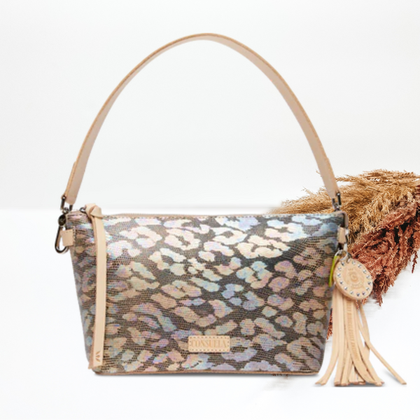 Iridescent, multicolor leopard print purse. This purse includes a light tan purse strap and a light tan tassel charm. This purse is pictured on a white background with pompous grass in the background.