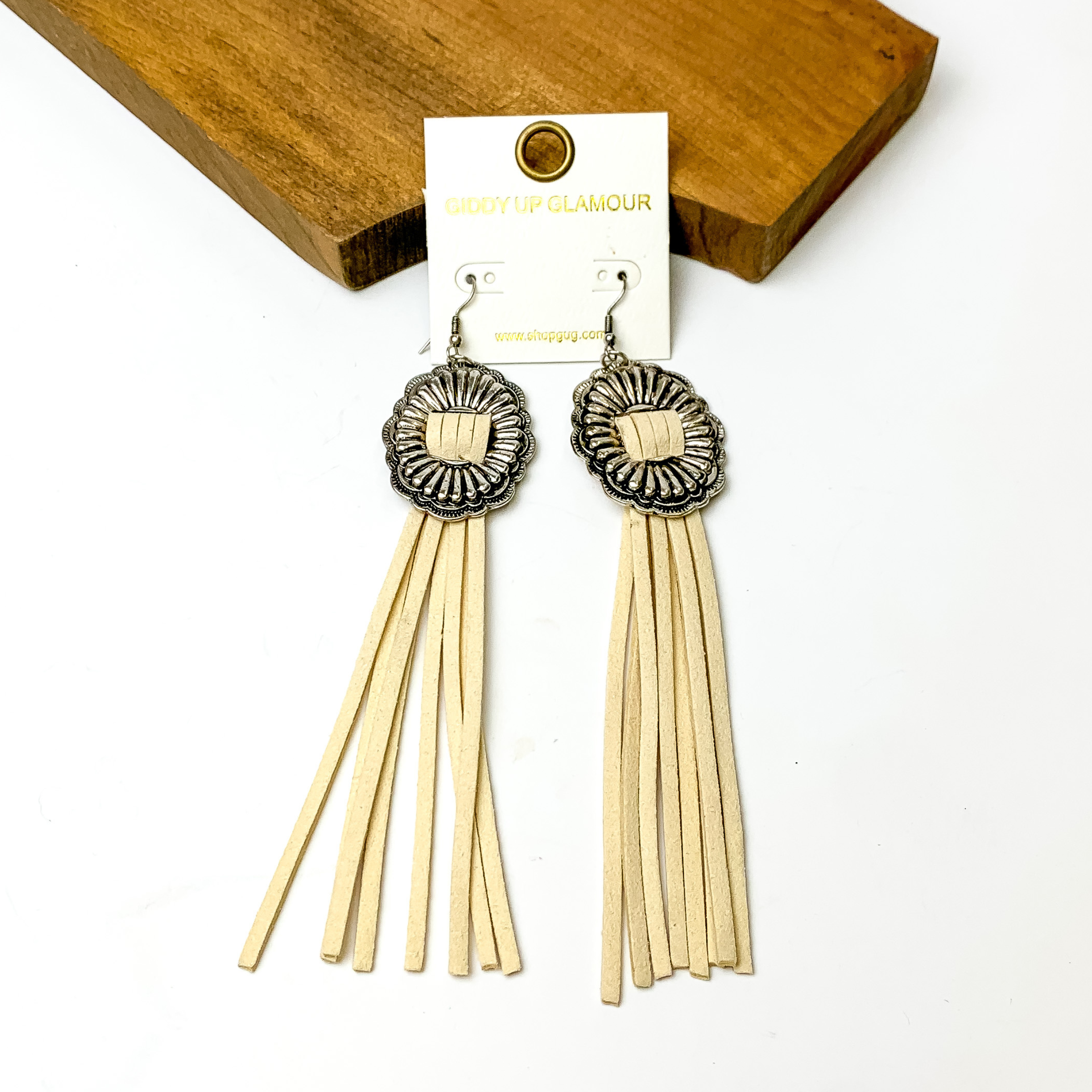 Silver concho dangle earrings with ivory tassels. These earrings are pictured on a white background with a brown block at the top of the picture.
