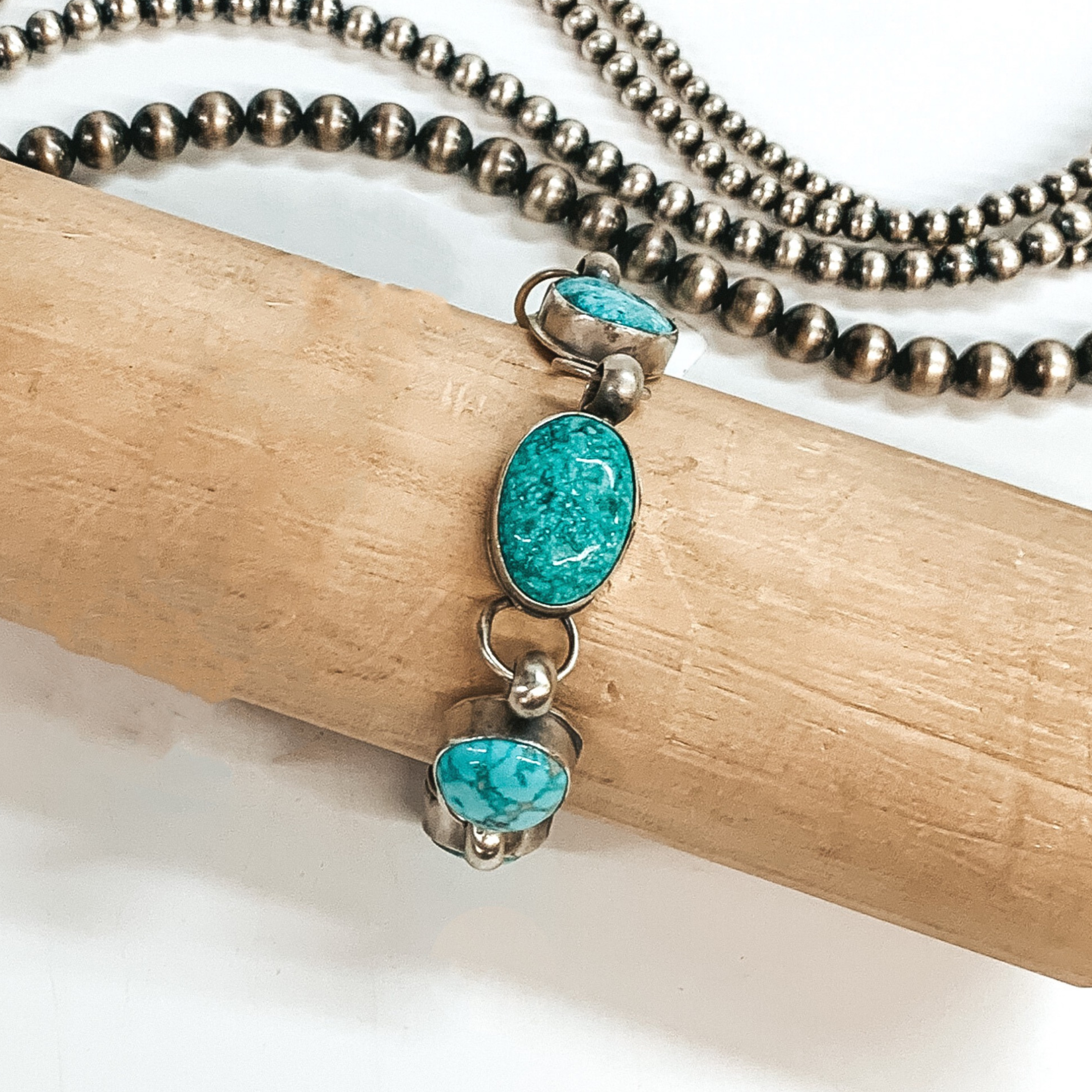 One sterling silver chain link bracelet with turquoise stones. This bracelet are pictured in a brown bracelet holder on a white background with silver beads behind it.