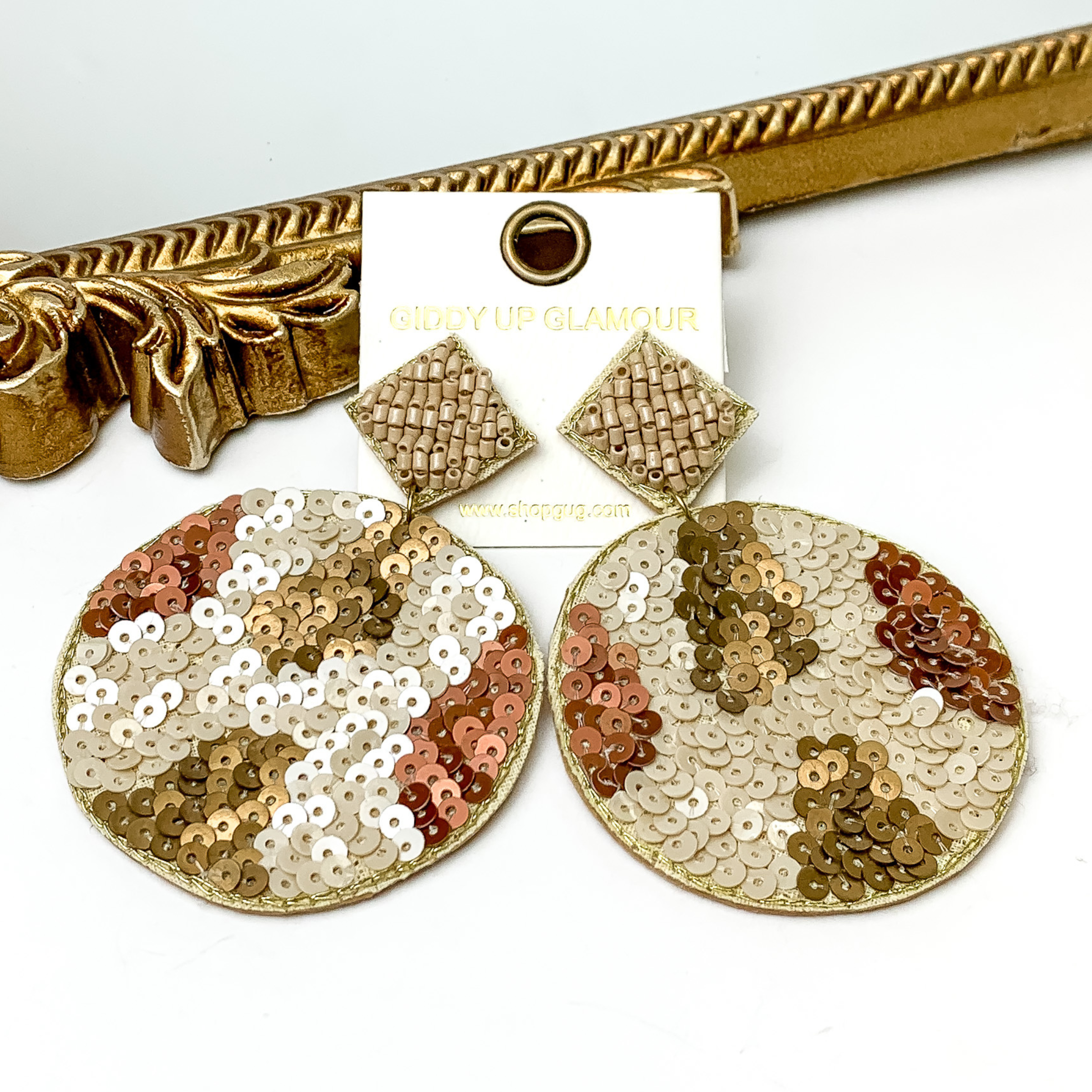 These are diamond post back, beige beaded earrings with a sequin beaded circle drop. These earrings include random spot pattern with bronze sequins, rust sequins, and nude sequins. These earrings are pictured in front of a gold mirror on a white background. 