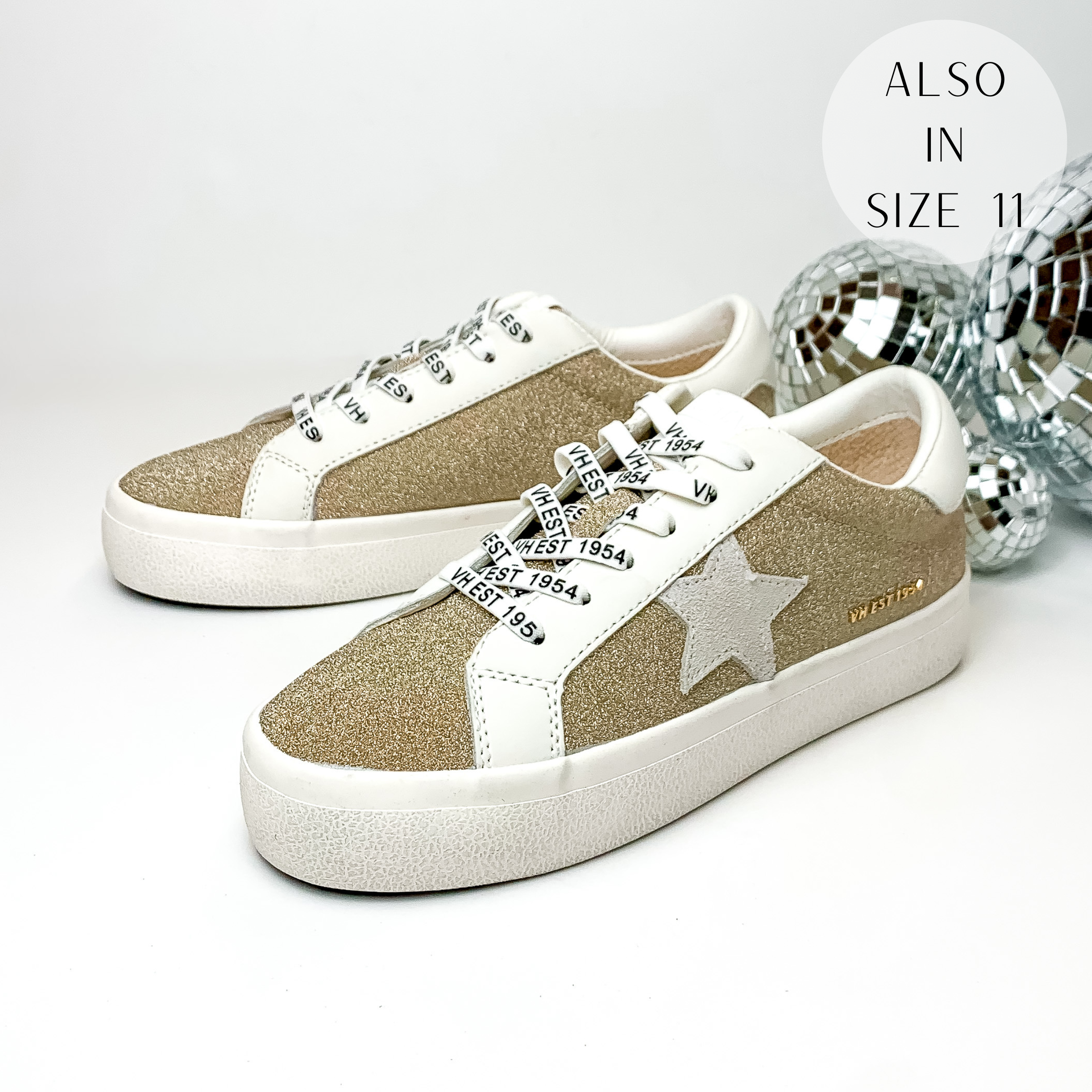Pitured are white tennis shoes with a light gold, sparkle inlay, and a grey star emblem. These shoes are pictured on a white background with disco balls behind them.