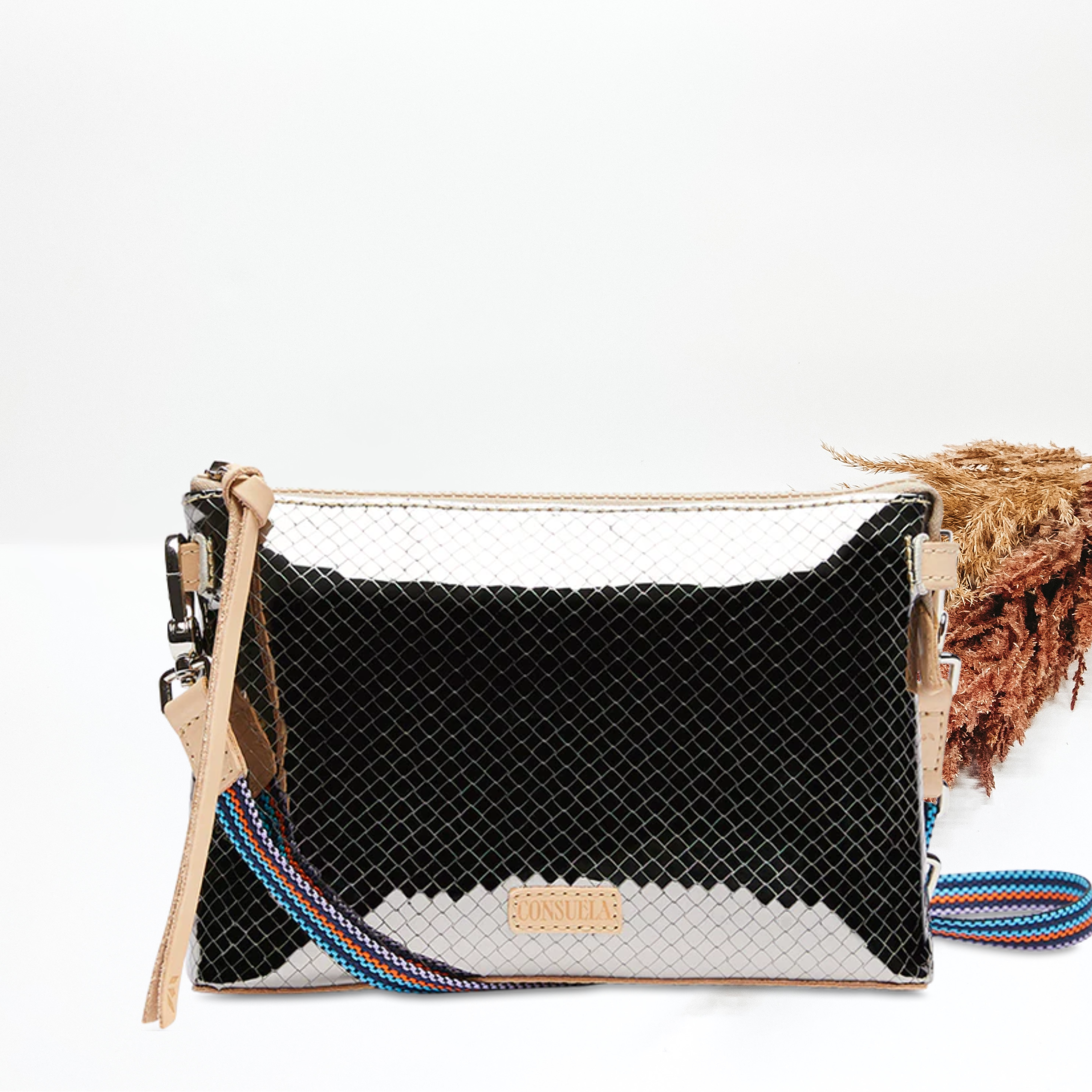 Pictured is a rectangle crossbody purse. This purse is silver with a stitched print design. This purse is pictured on a white background with pompous grass on the right side of the picture.