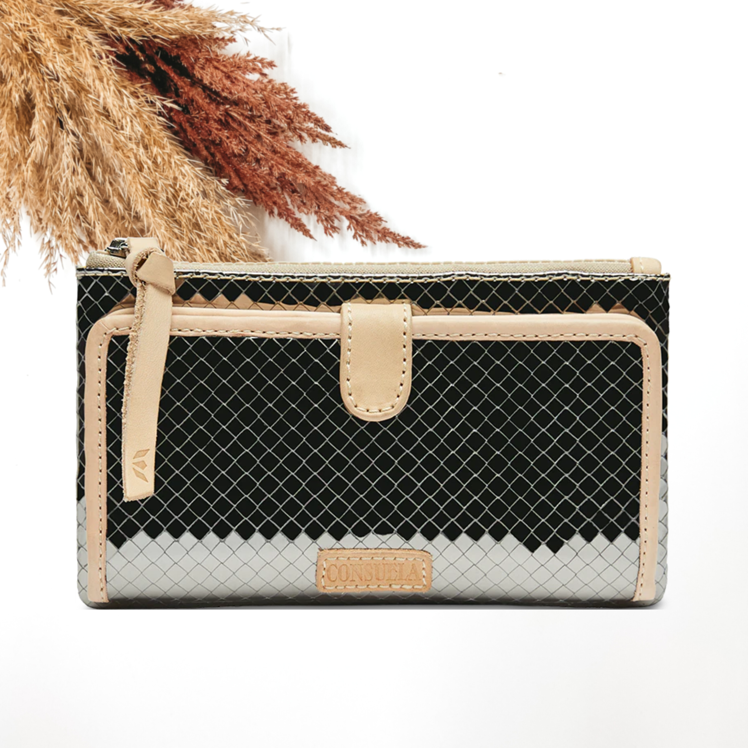 Pictured is a rectangle wallet that has a silver, gunmetal stitched print design. This wallet includes a front flap with a light tan outline and a top zipper with a light tan zipper pull. This wallet is pictured on a white background with pompous grass in the top left corner.
