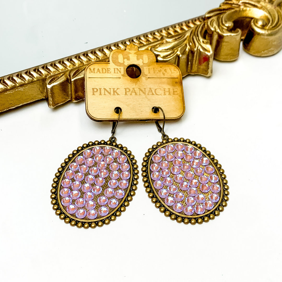 Bronze oval drop earrings with a bronze beaded outline. These earrings have an inlay of lavender crystals. These earrings are pictured on a white background.