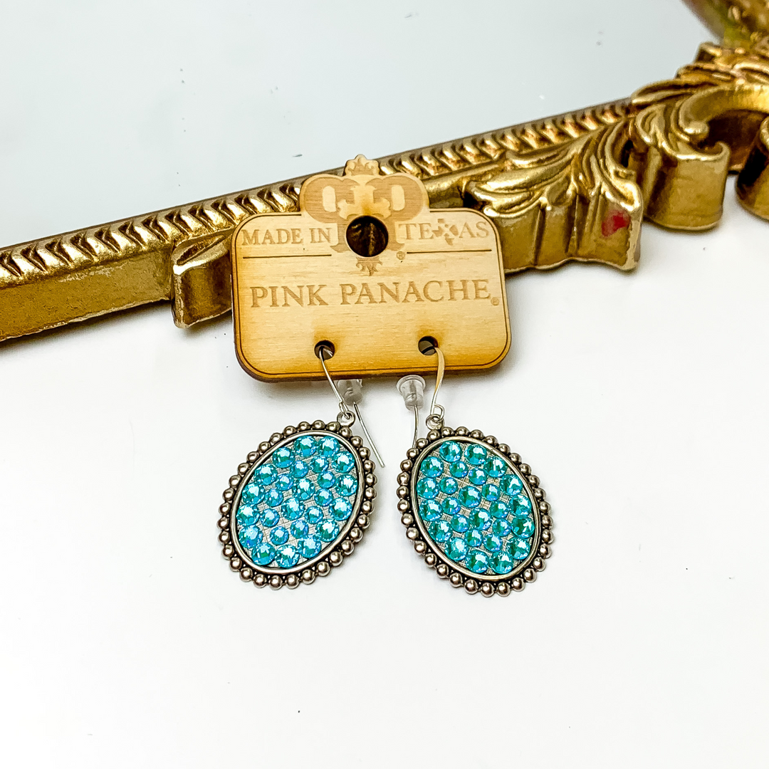 Silver oval drop earrings with a silver beaded outline. These earrings have an inlay of laguna delight crystals. These earrings are pictured on a white background. 