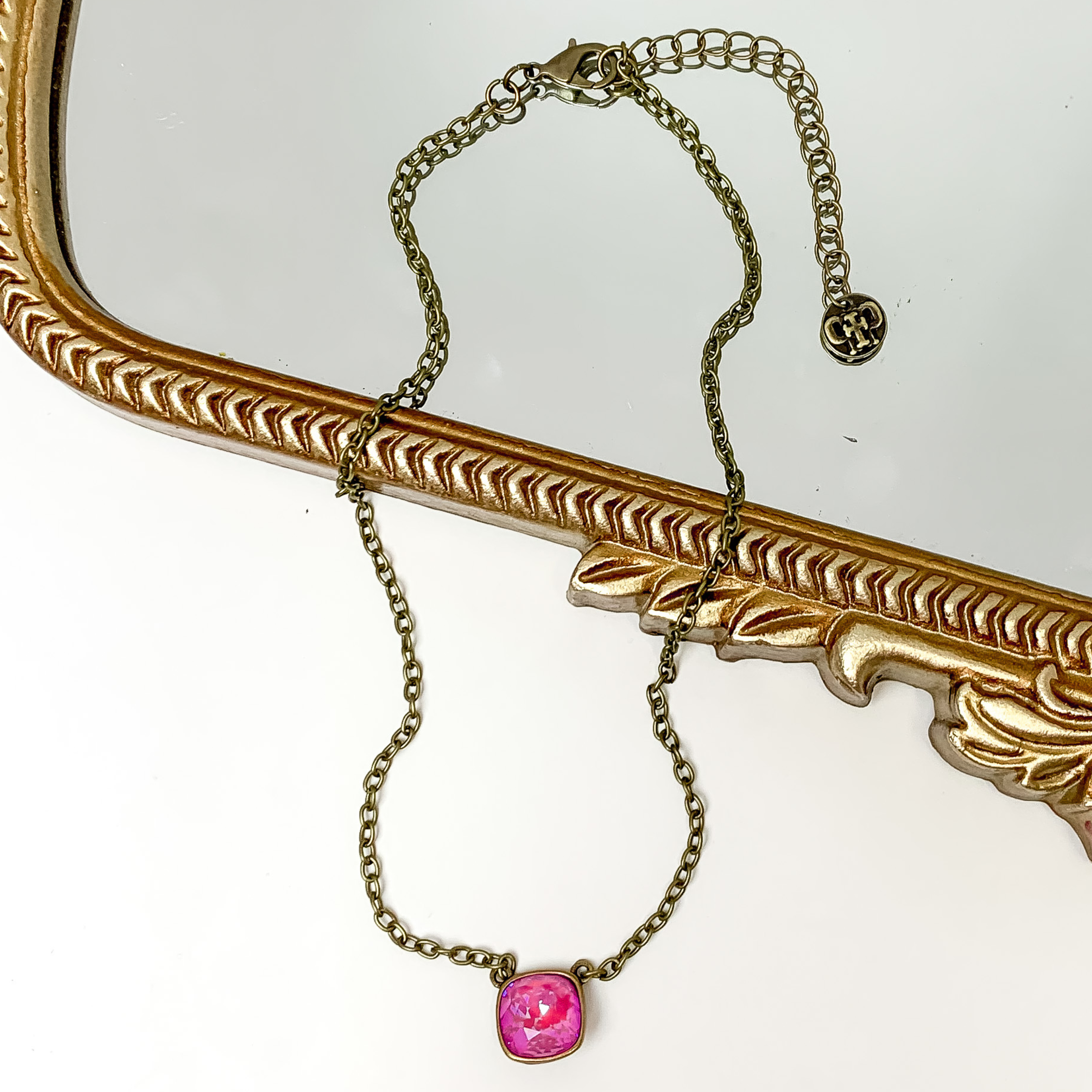 Bronze chain necklace with a pink lotus delight cushion cut crystal. This necklace is pictured partially laying on a gold mirror on a white background.