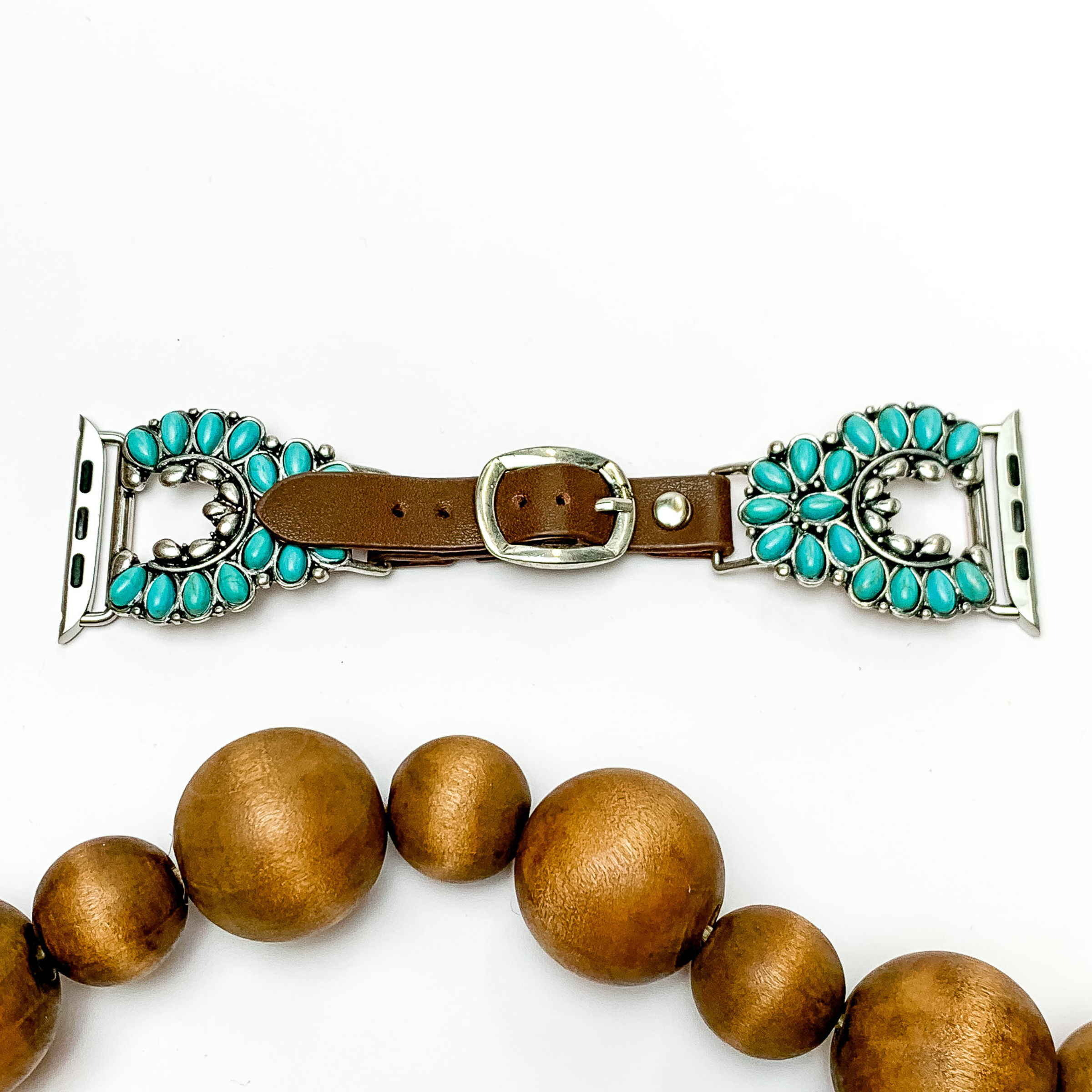 Dark Brown watch band with silver, naja ends and turquoise stones with Apple watch band acessories. This watch band is pictured on a white background with brown beads underneath the band. 