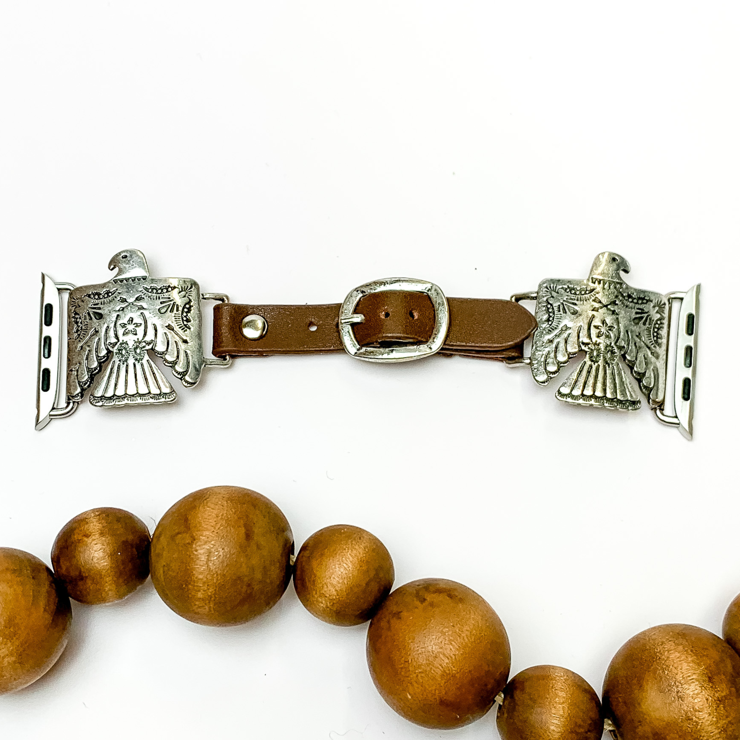 Dark Brown watch band with silver, engraved thunderbird pendants and Apple watch band acessories. This watch band is pictured on a white background with brown beads underneath the band. 