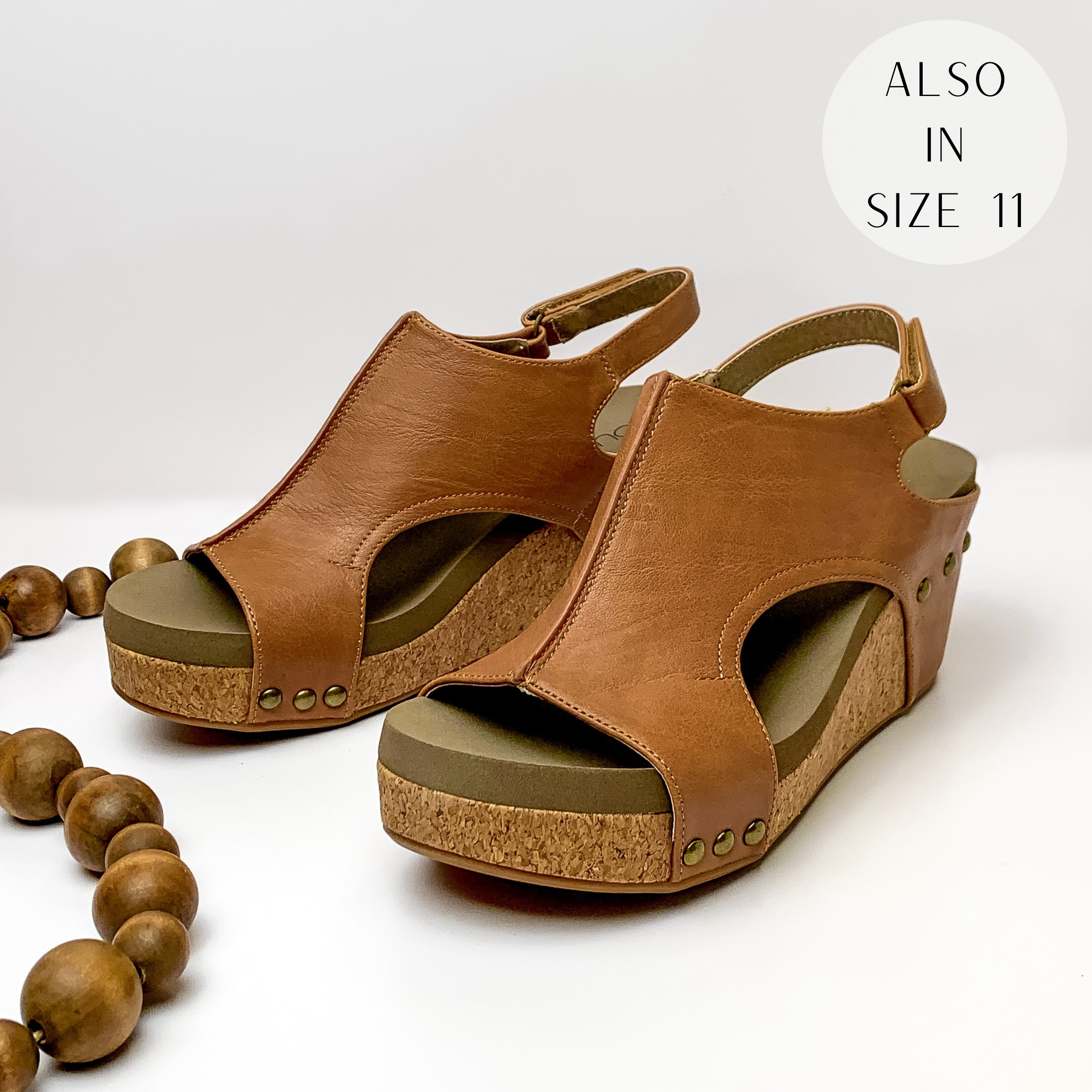 Cork wedges with a cognac color upper with bronze studs connecting the upper to the wedge. These wedges also include a velco strap. These wedges are pictured on a white background with brown beads on the left side of the boots.