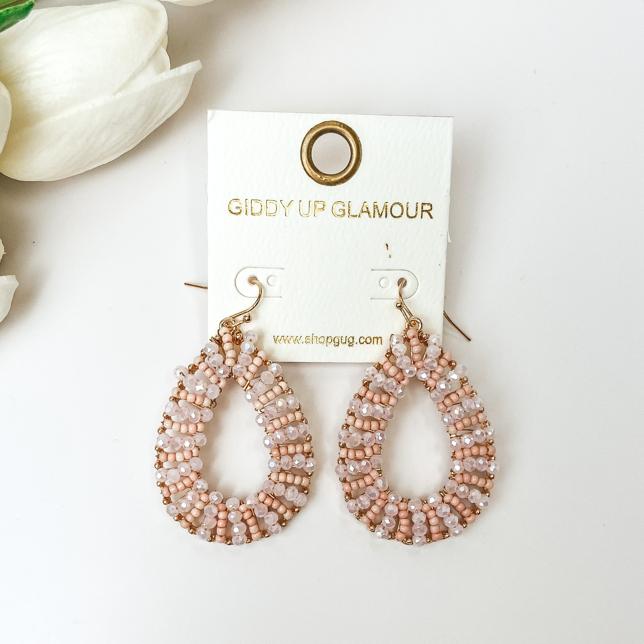 Light pink and gold teardrop earrings on a white background with white flowers.