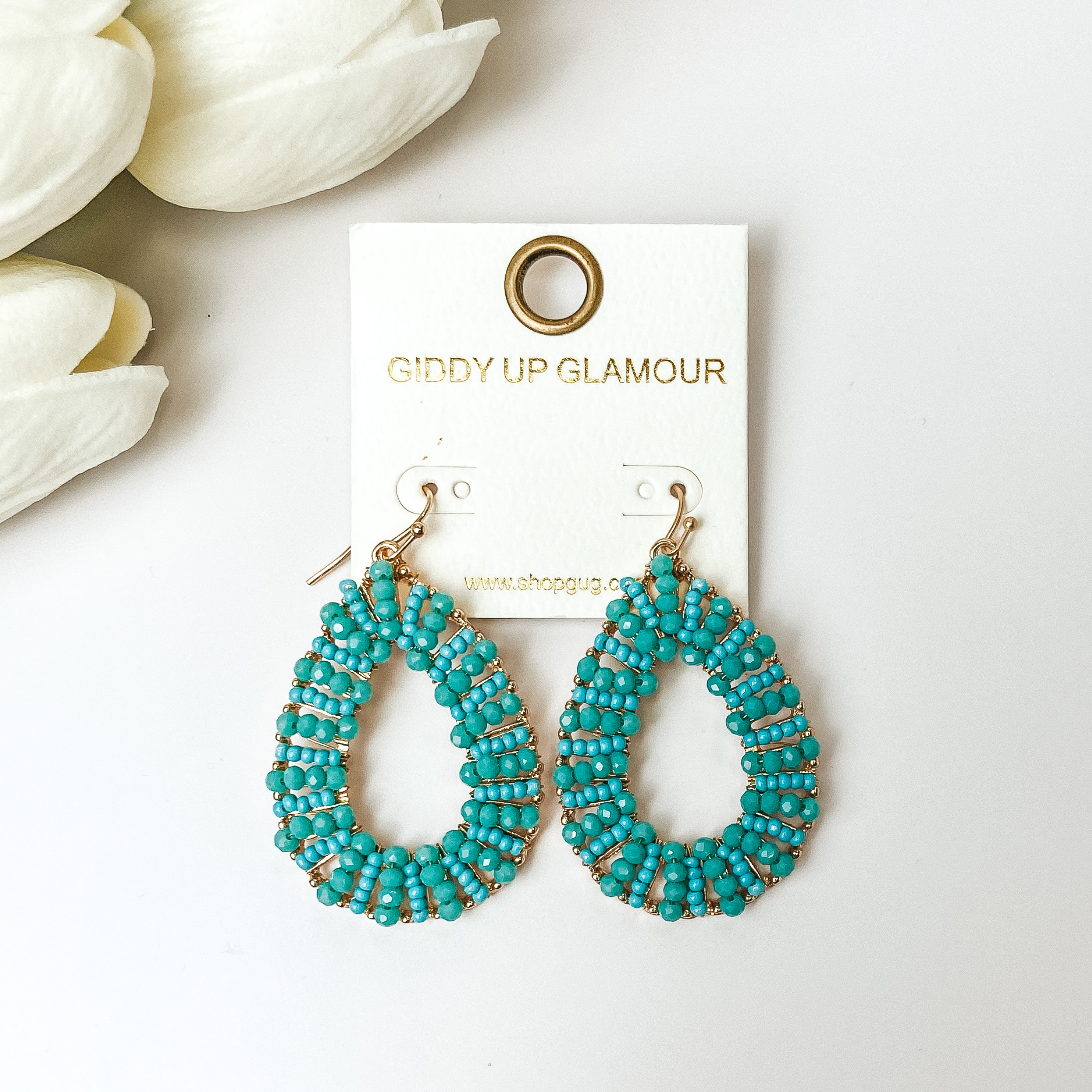Turquoise Teardrop earrings with gold undertones on a white background with white flowers.