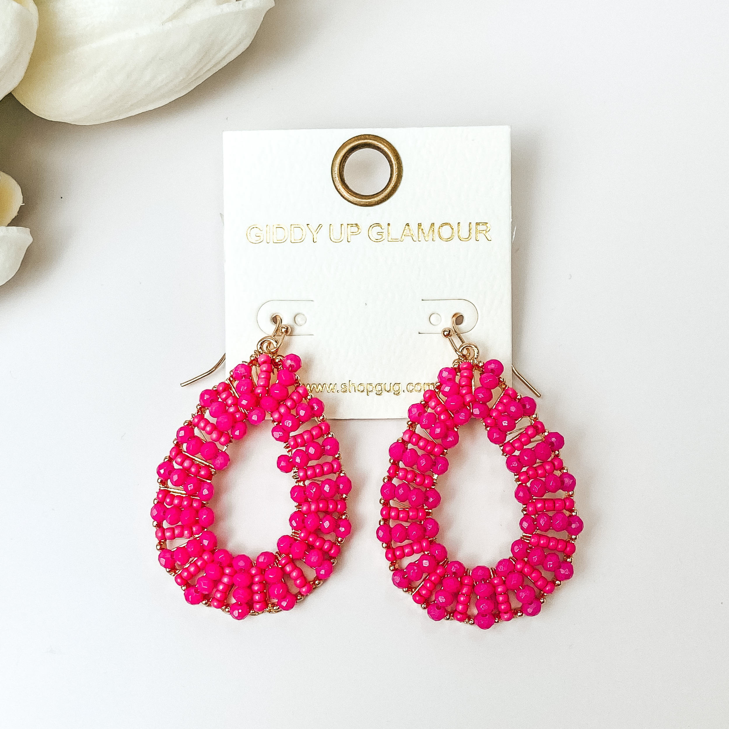 Gold undertone teardrop earrings with hot Pink Beads on a white background with white flowers.