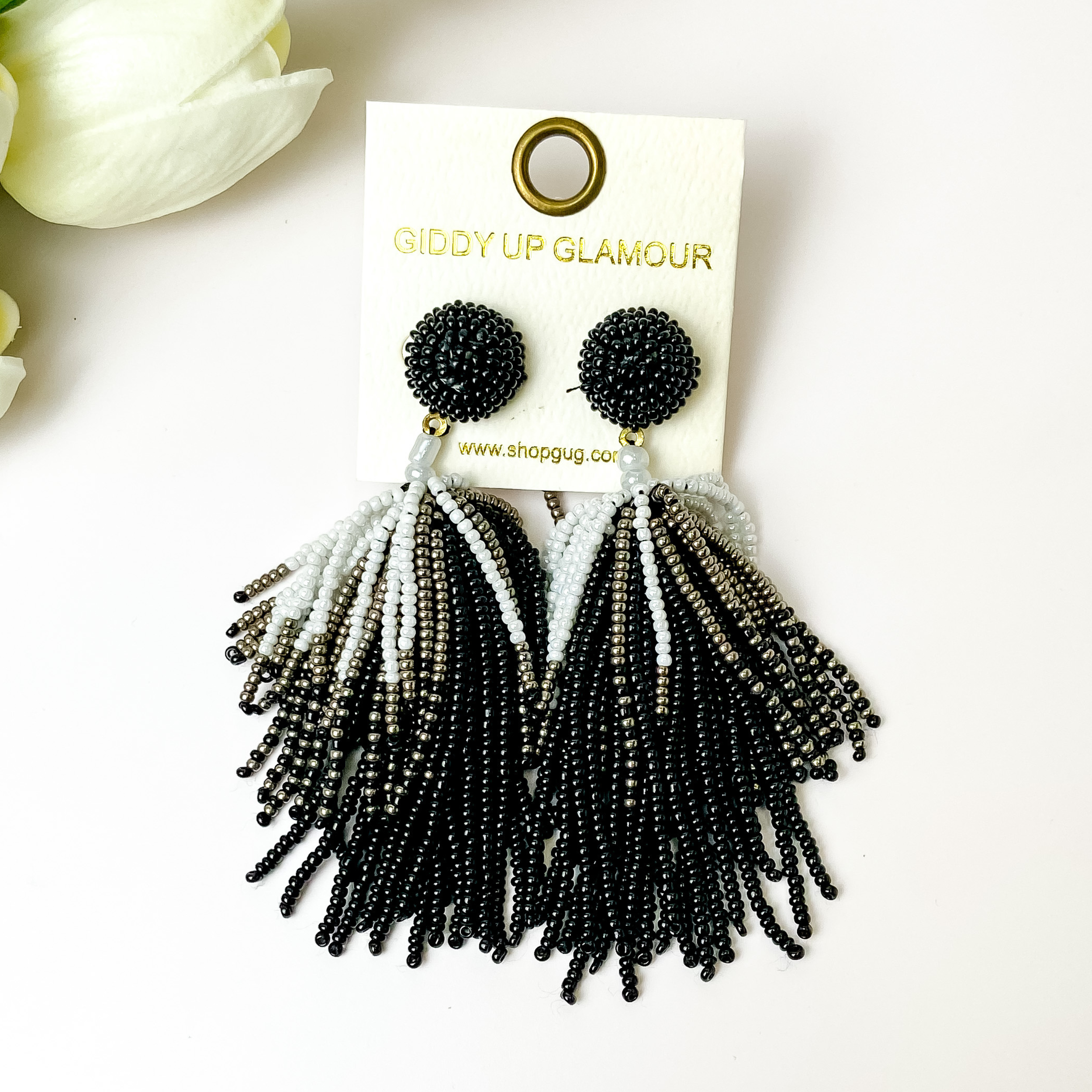 Black, white, and silver beaded tassel earings on a white background with white flowers.