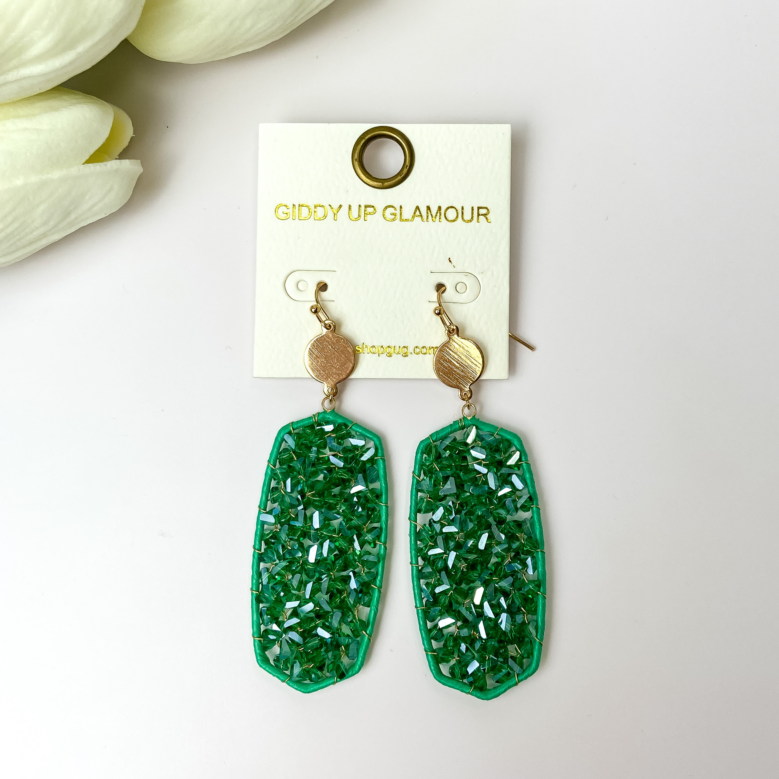 Emerald green crystal earrings with gold tone accents on a white background with white flowers in the corner.