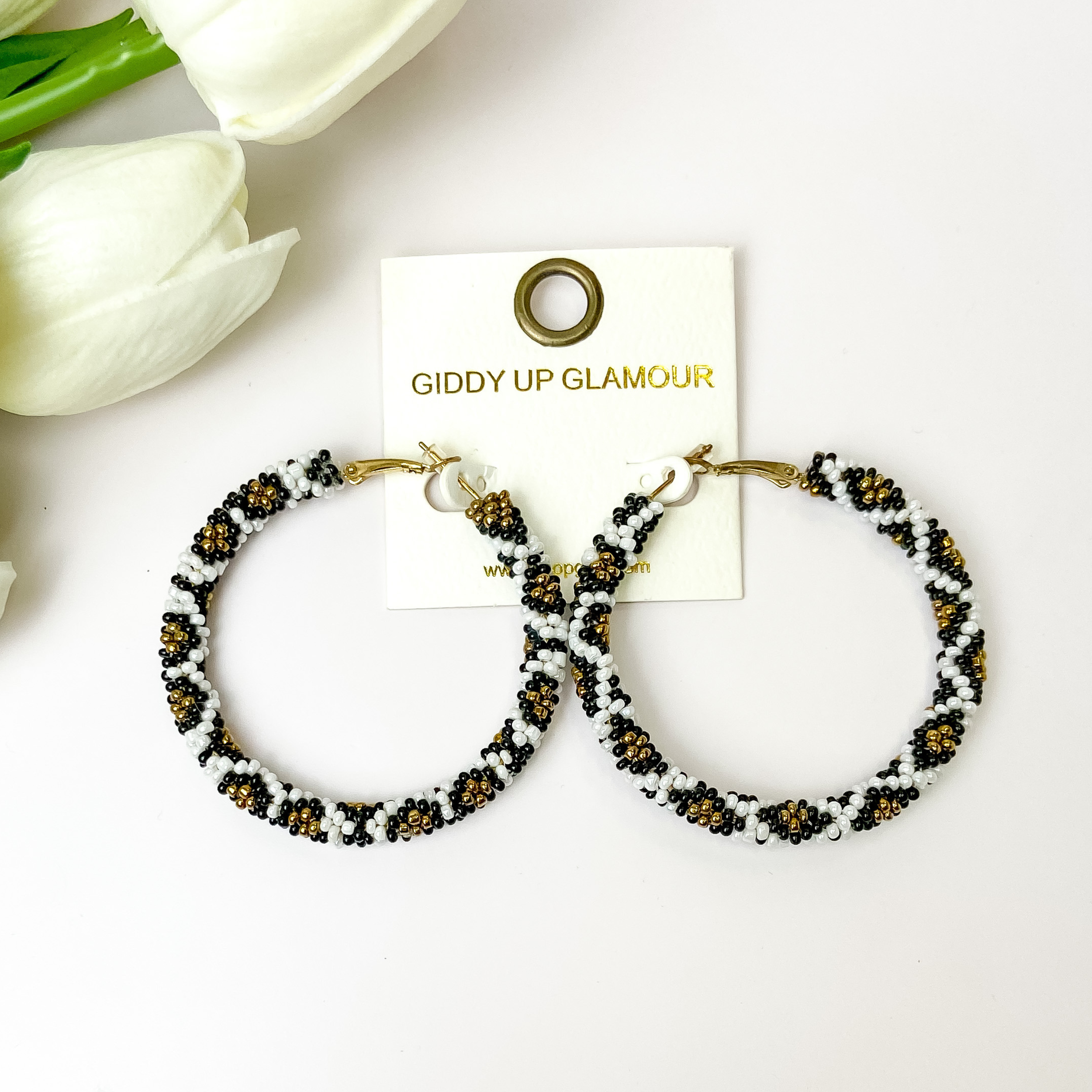 White, black, and gold pattern beaded hoops on a white background with white flowers in the corner.